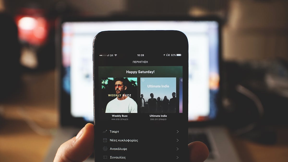 8 Entertainment Trends That Are Ruining American Pop Culture 4 A person holding a smartphone with music streaming app in front of a laptop screen indoors.