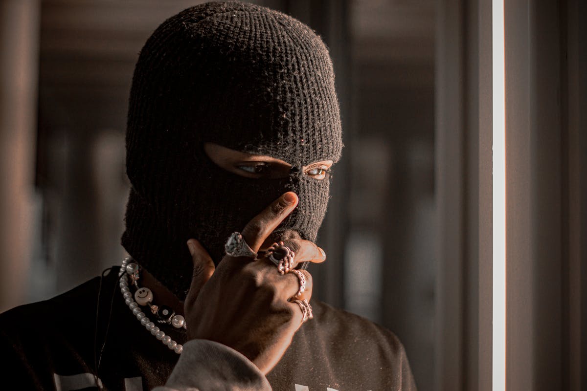 A person wearing a black balaclava adorned with rings and necklaces, creating an air of mystery.