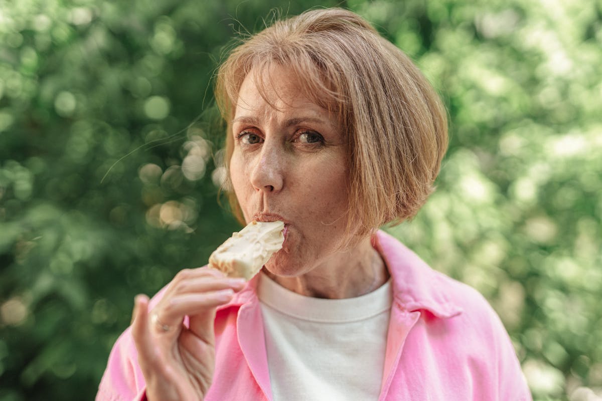 A senior woman outdoors, savoring a delicious ice cream bar on a sunny day.