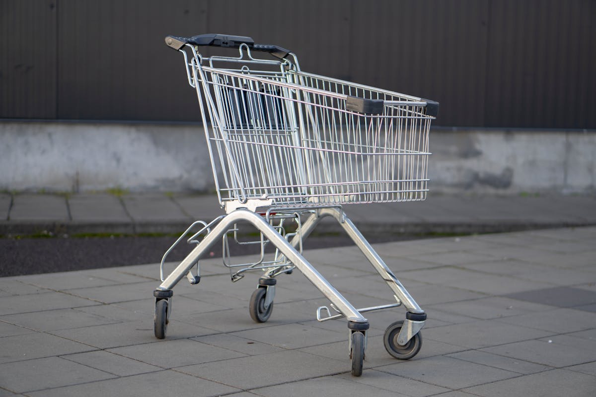 8 Recession Red Flags That Should Worry Americans Right Now 2 A solitary metal shopping cart stands in an empty outdoor parking lot, capturing the essence of consumerism.