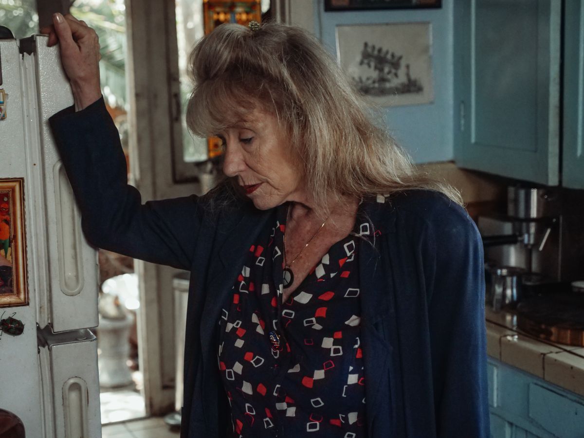 8 Signs You’re Being Too Frugal in Retirement 2 A thoughtful senior woman leans on a refrigerator, evoking emotion and nostalgia in a cozy kitchen setting.