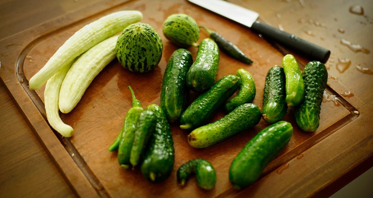 A variety of fresh cucumbers arranged on a wooden chopping board with a knife.