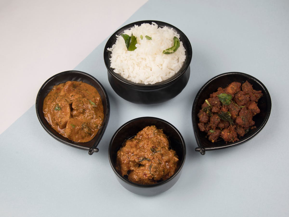 A variety of Indian dishes featuring rice, curry, and fried meat served in black bowls.