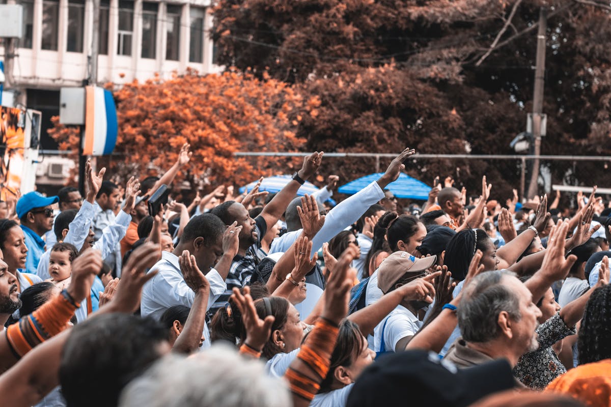 A vibrant outdoor gathering with people raising hands in unity, set in an urban environment.