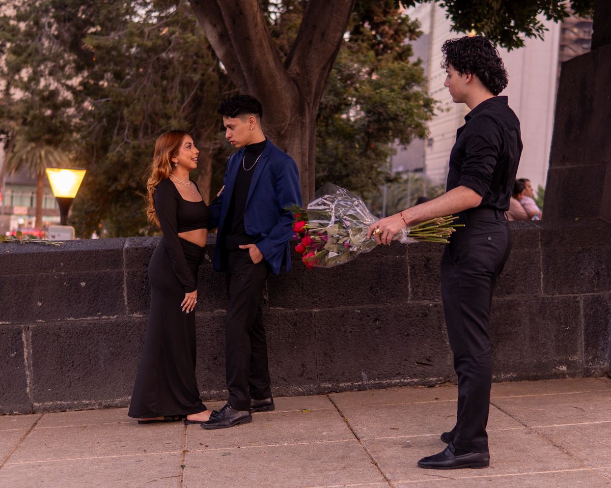 A woman and two men in an intriguing love triangle scenario with roses outdoors.