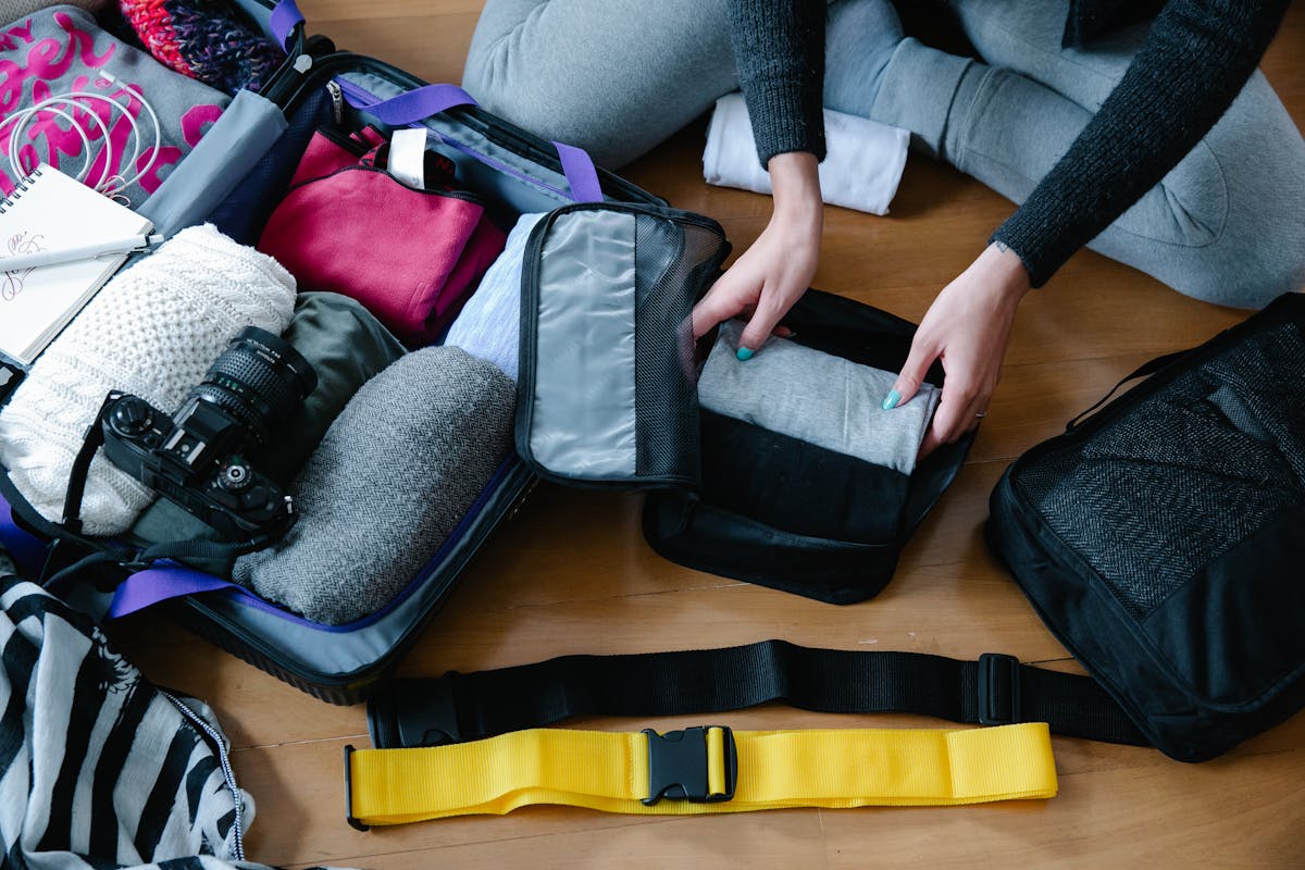 10 Major Travel Struggles and How We Can Make Every Trip Less Stressful 2 A woman arranging clothes and accessories into a suitcase, preparing for travel.