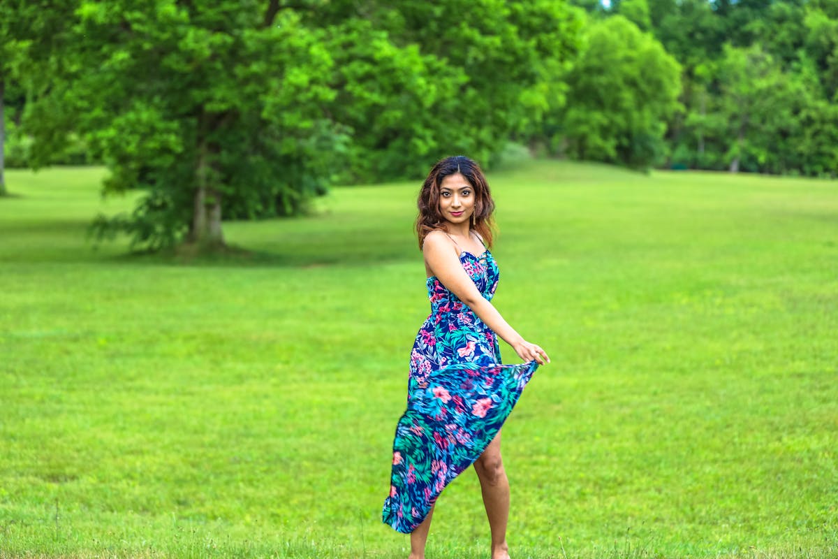 A woman in a colorful sundress poses elegantly in a vibrant green park setting.