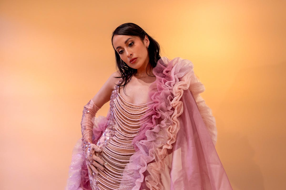 7 Reasons “Mogging” Is Everywhere and Why That Could Be a Problem 2 A woman in a pink ruffled dress posing against a warm background, exuding elegance and style.