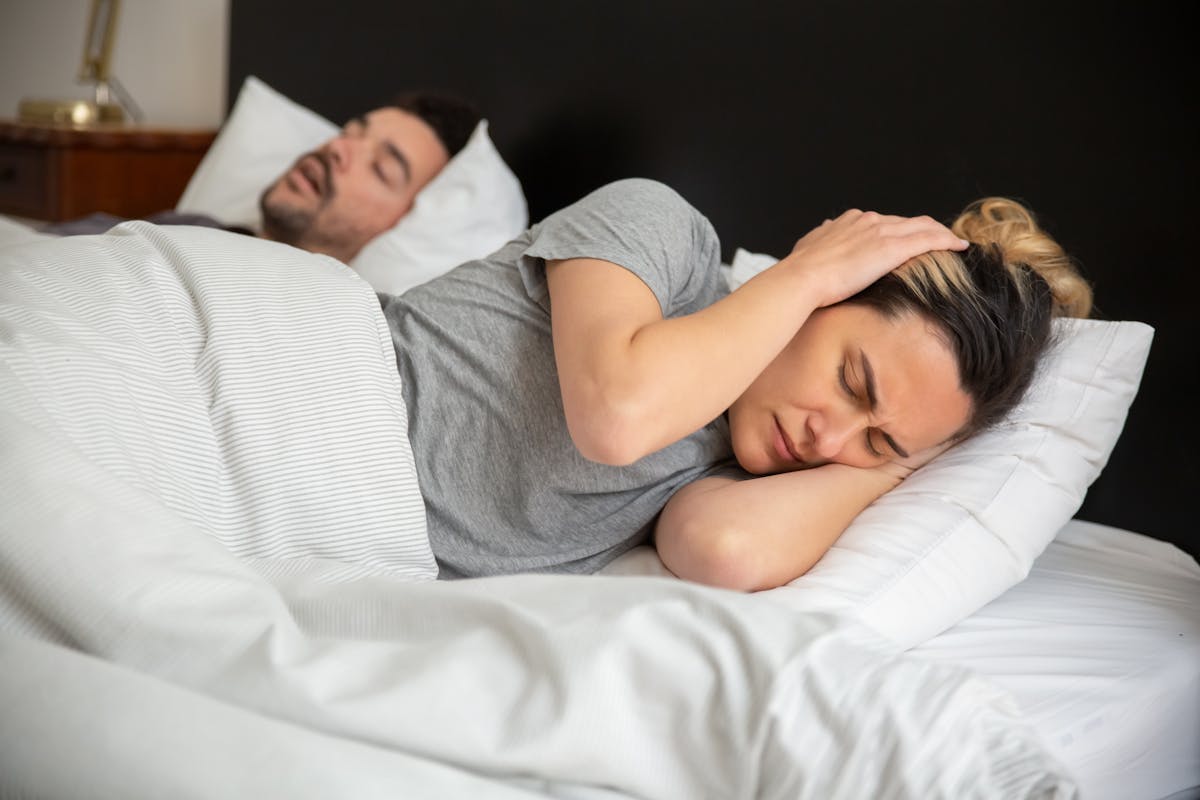 10 Ways Snoring Is Secretly Ruining Your Life 3 A woman looks frustrated in bed as her partner snores loudly, highlighting sleep disturbance issues.