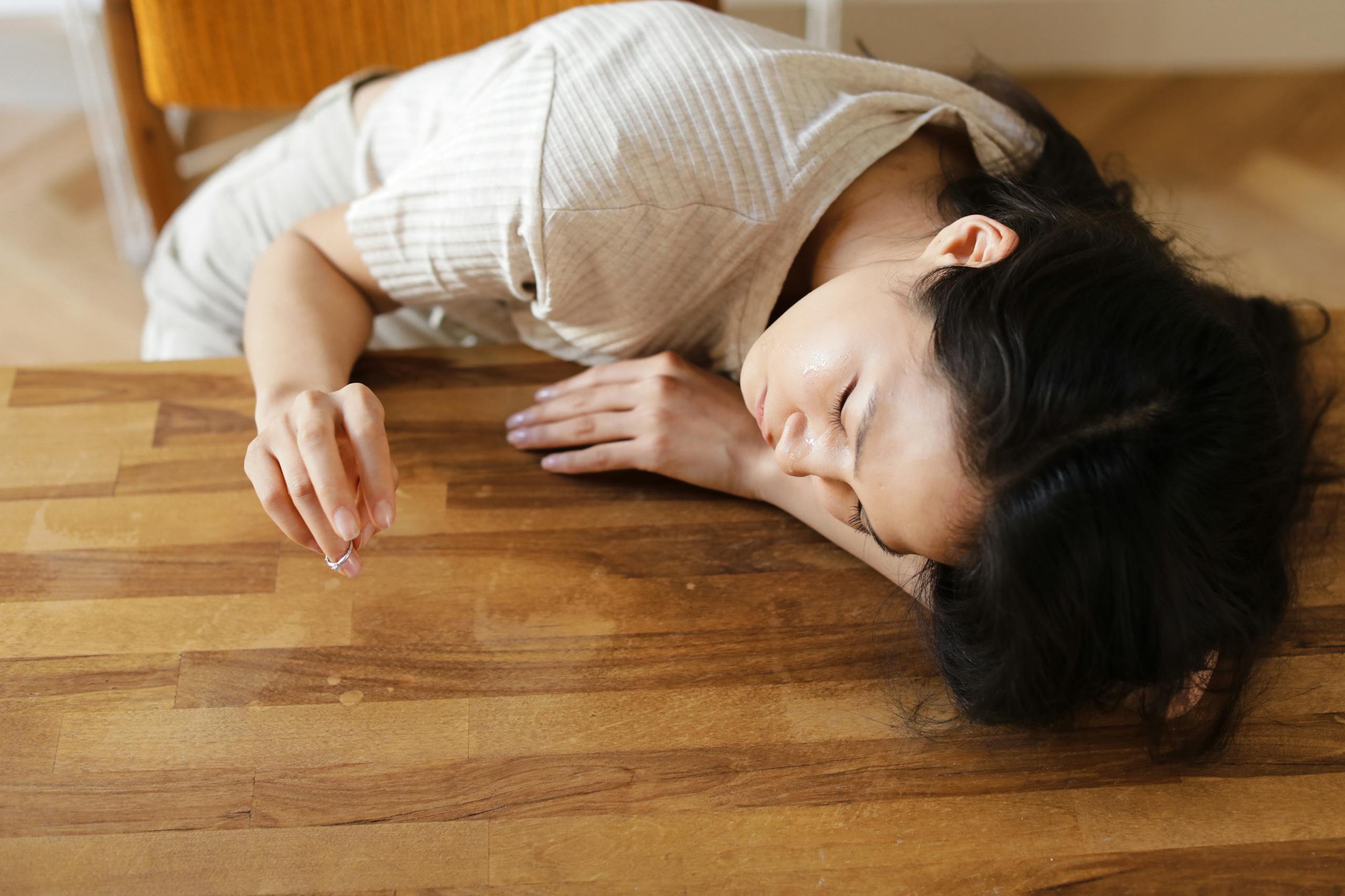 7 Shocking Ways Heartbreak Changes People Permanently 3 A woman lying sadly at a wooden table, holding a wedding ring, conveying emotions of separation and loss.