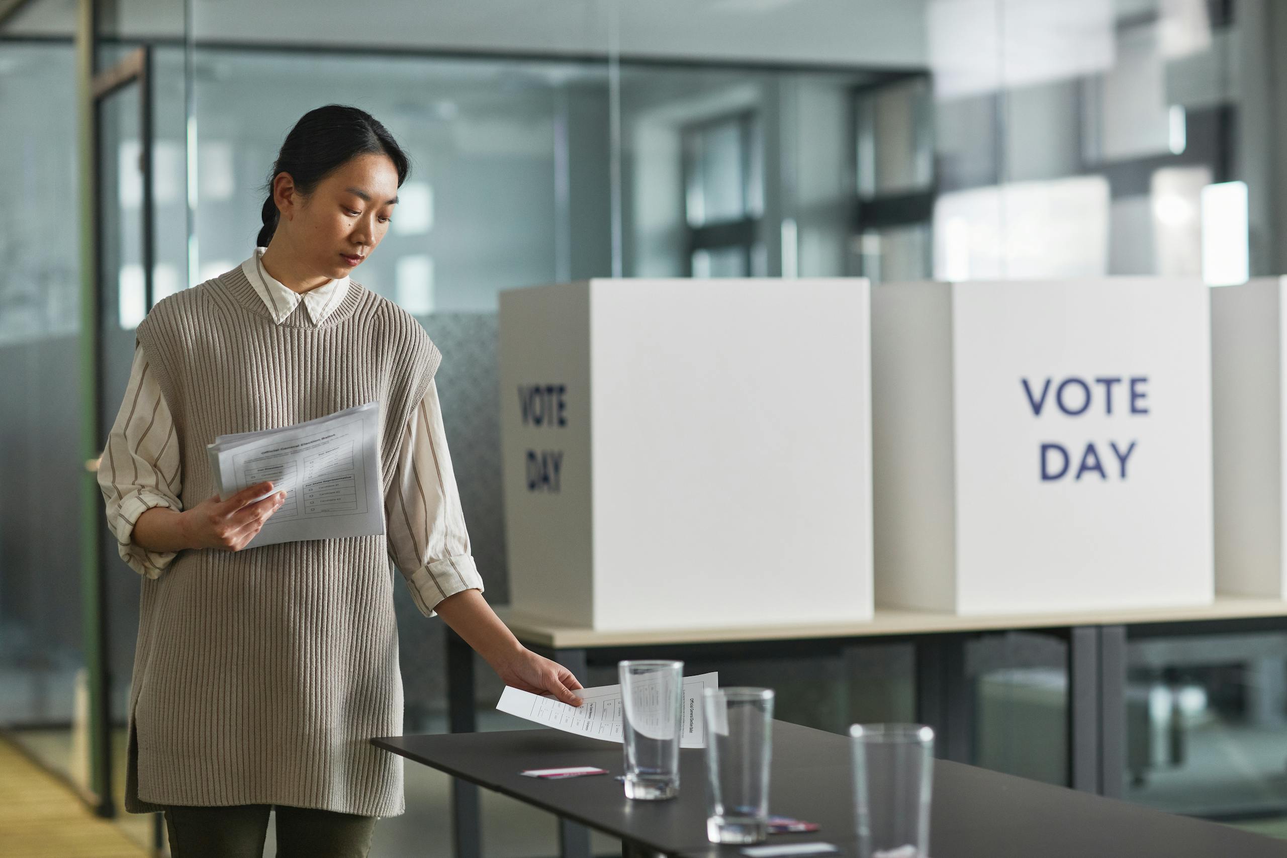 7 Warning Signs the 2026 Midterms Are Already Turning Ugly 3 A woman organizing ballot papers indoors at a voting station on election day.