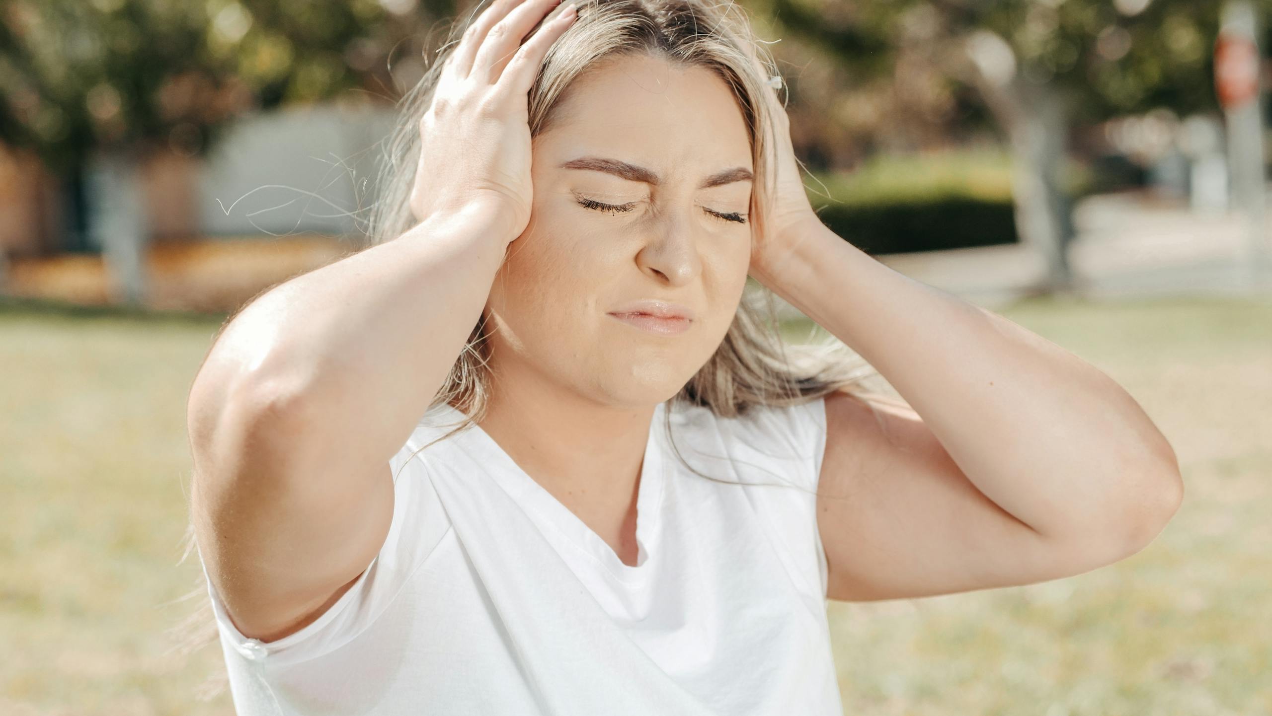 7 Reasons Botox After Pregnancy Can Become a Beauty Decision You Regret 2 A woman outdoors holds her head, depicting stress or a headache.