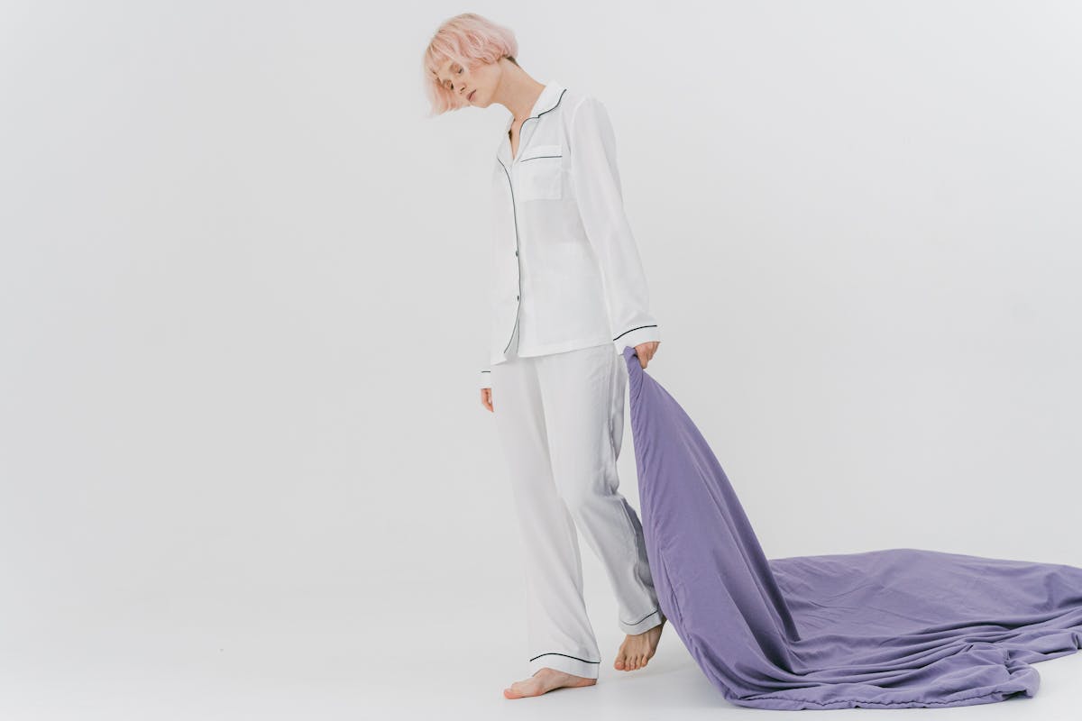 7 Sleep Problems That Could Signal Dementia Early 4 A woman wearing pajamas drags a purple blanket in a minimalist studio setting.