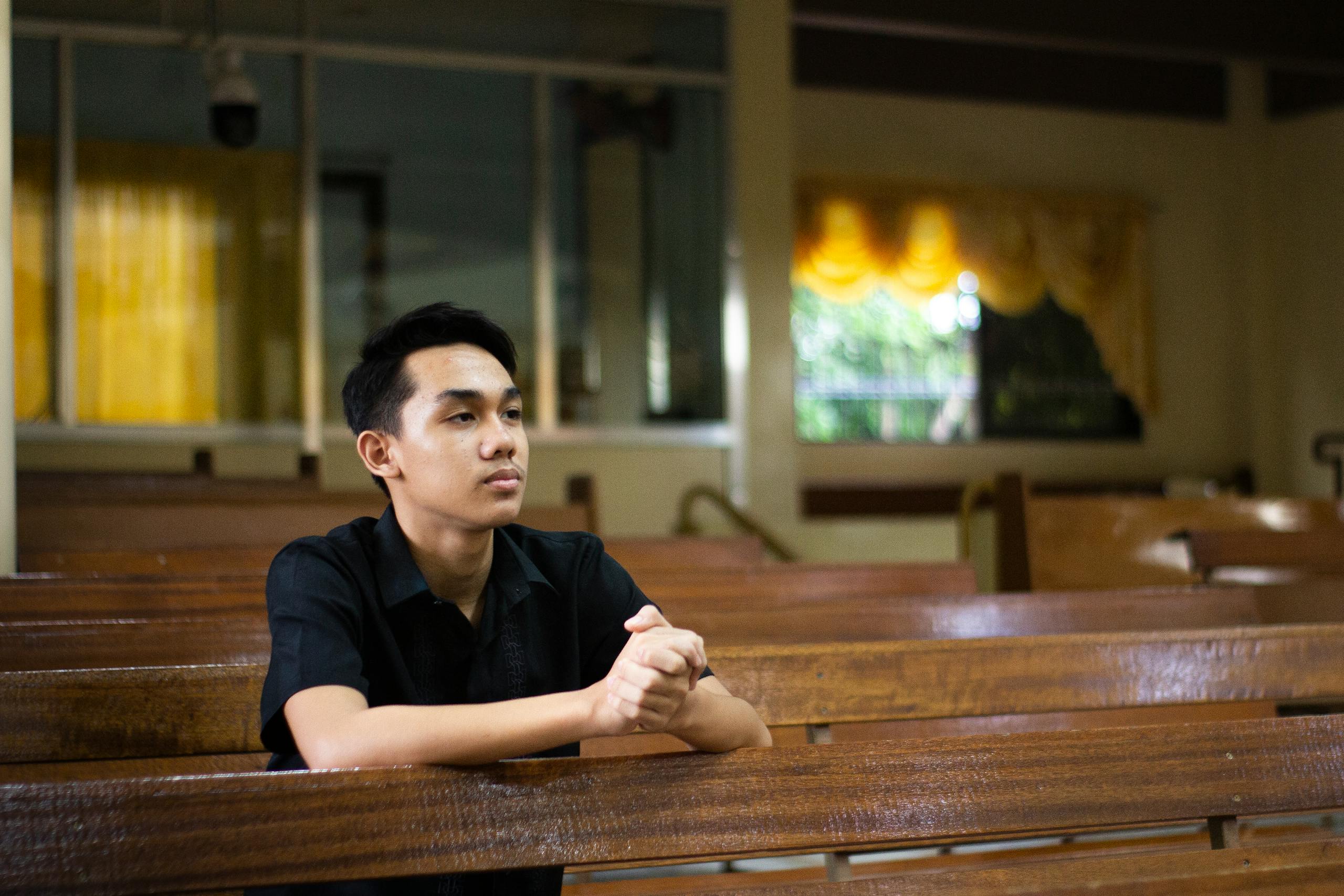 10 Harsh Truths About Why Church No Longer Feels Like Home to Some Americans 3 A young man in a church, sitting in a pew, clasping hands in prayer.