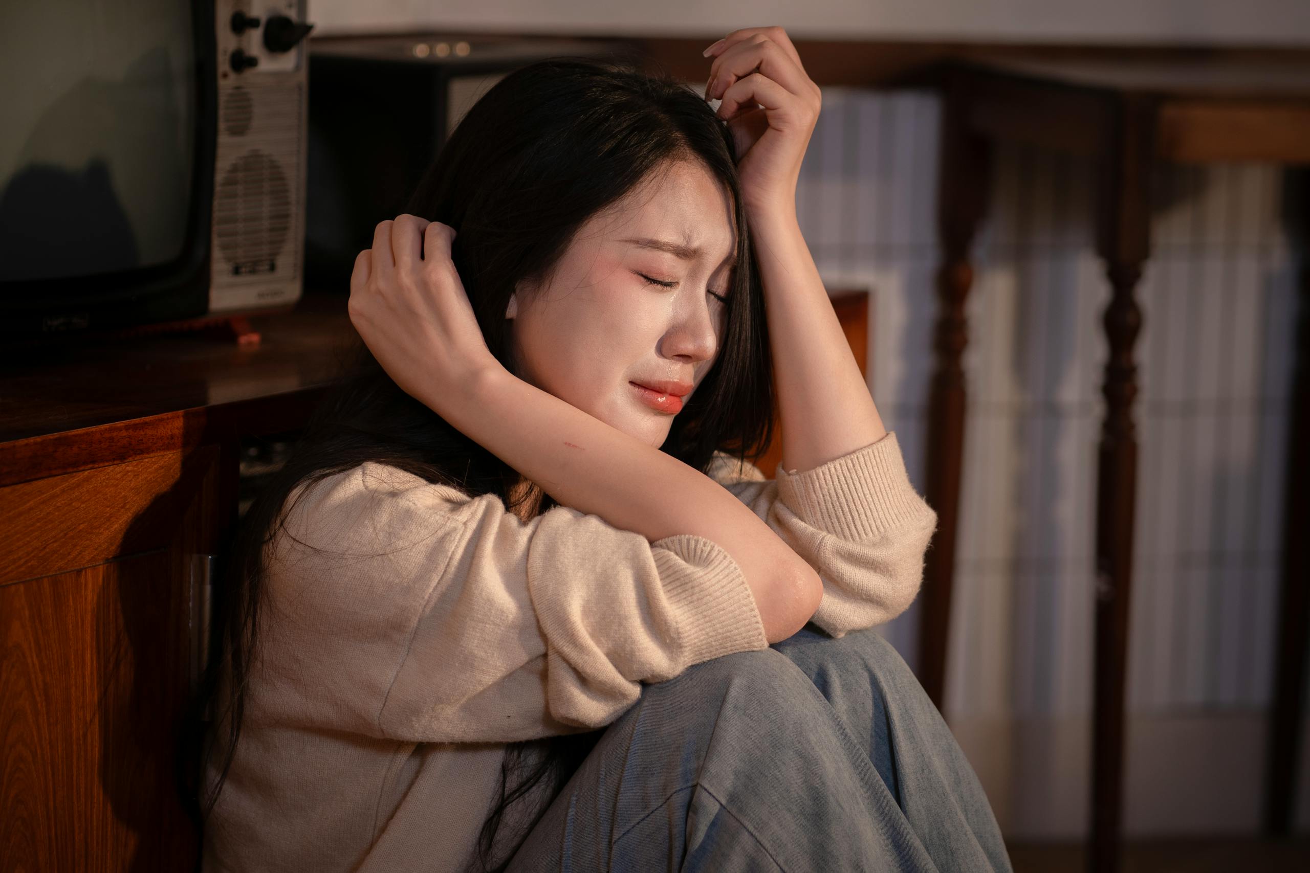 7 Shocking Ways Heartbreak Changes People Permanently 4 A young woman sitting indoors, expressing deep emotional distress.