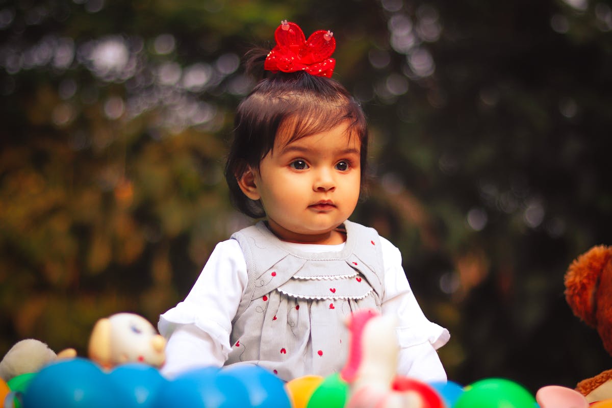 Adorable toddler girl with a red bow, playing with colorful toys in an outdoor setting.