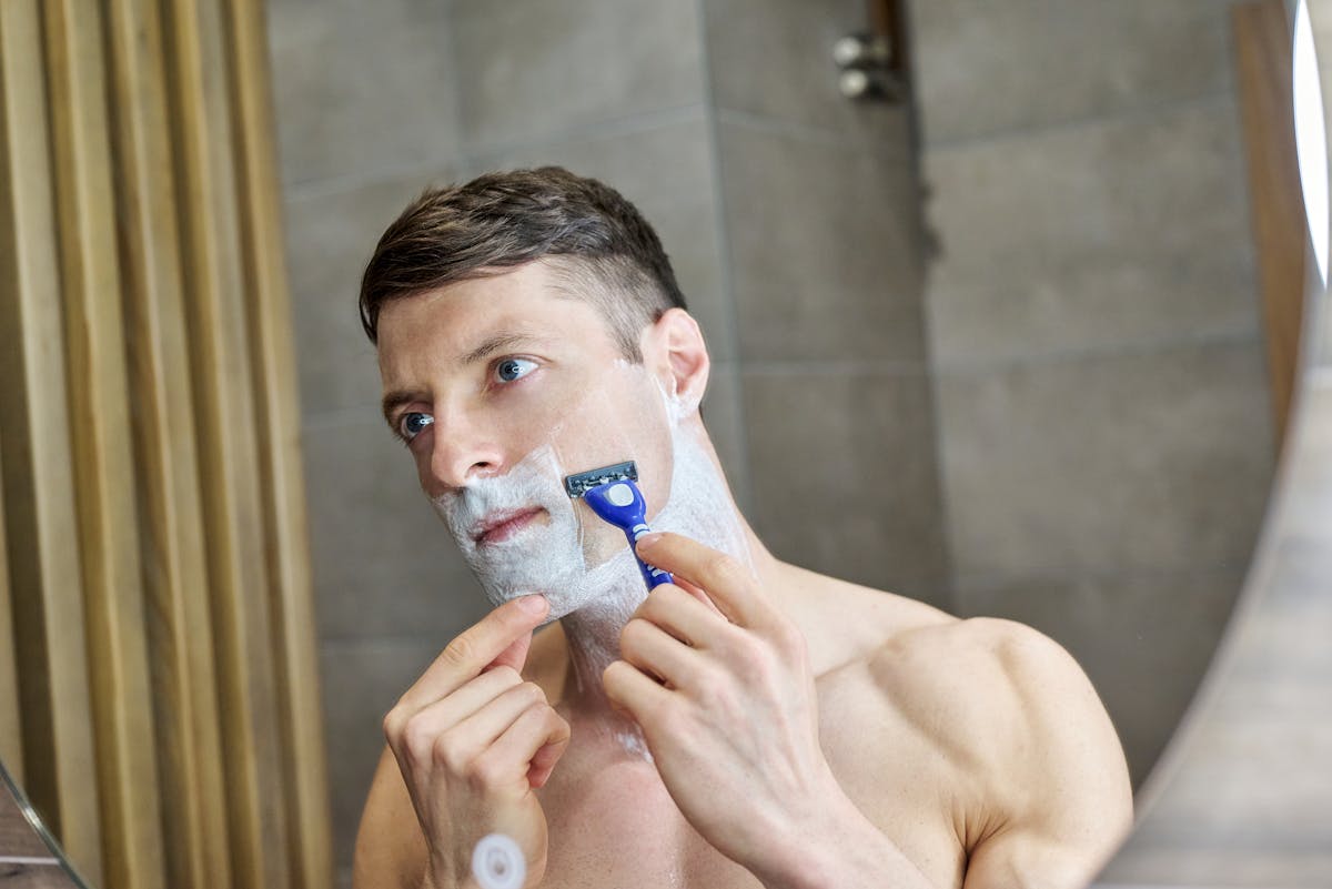 Adult man shaving in front of a mirror, focusing carefully with a razor and shaving cream.