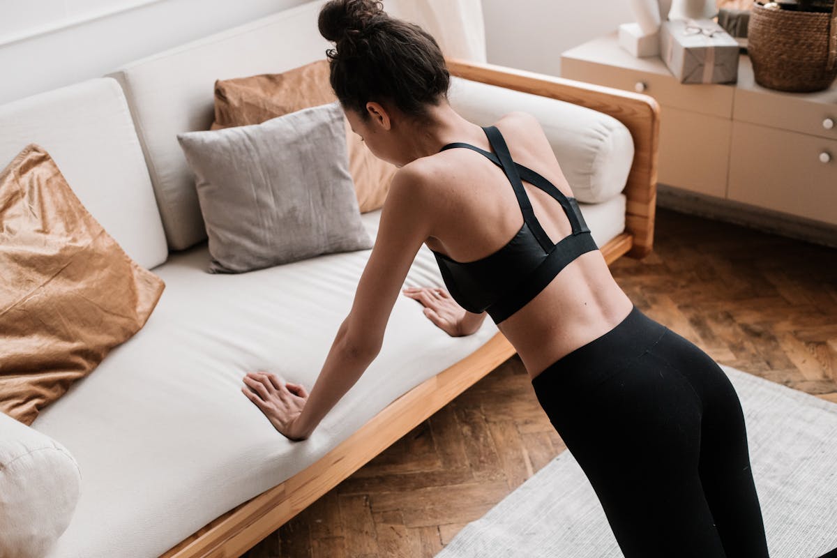 6 Self-Care Myths That Are Doing More Damage Than Most People Realize 1 An active adult woman performs push-ups indoors using a sofa for support, emphasizing a healthy lifestyle.