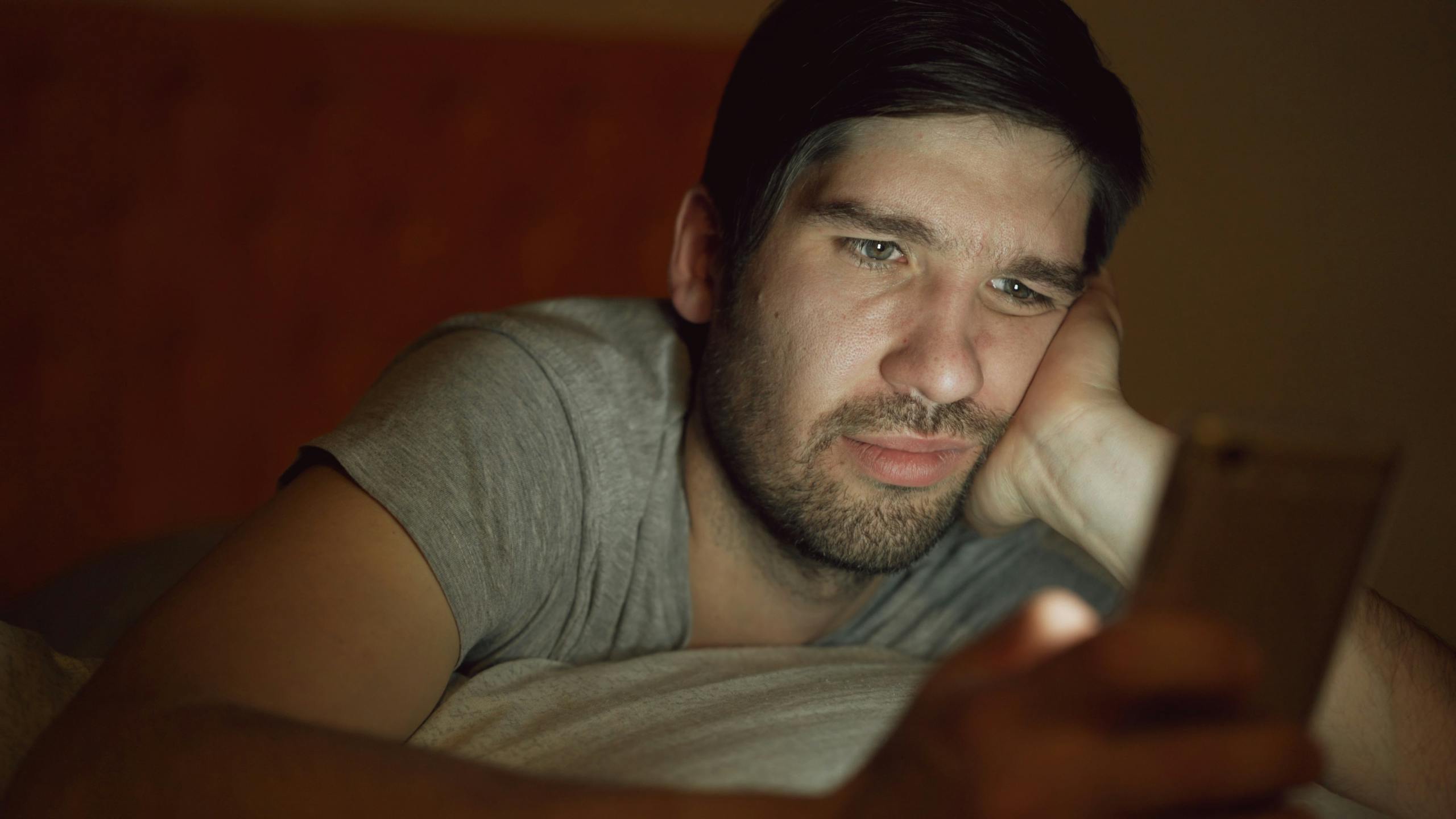8 Ugly Reasons Social Media Is Destroying Attention Spans 1 An adult man in a dim room looking at a smartphone with a thoughtful expression.
