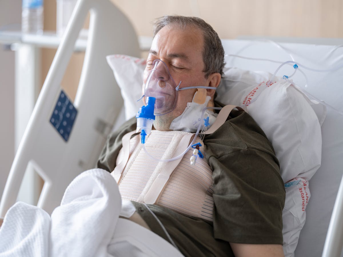 9 Silent Reasons People Die in Their Sleep, According to Science 3 An elderly man lies in a hospital bed wearing an oxygen mask for medical care.