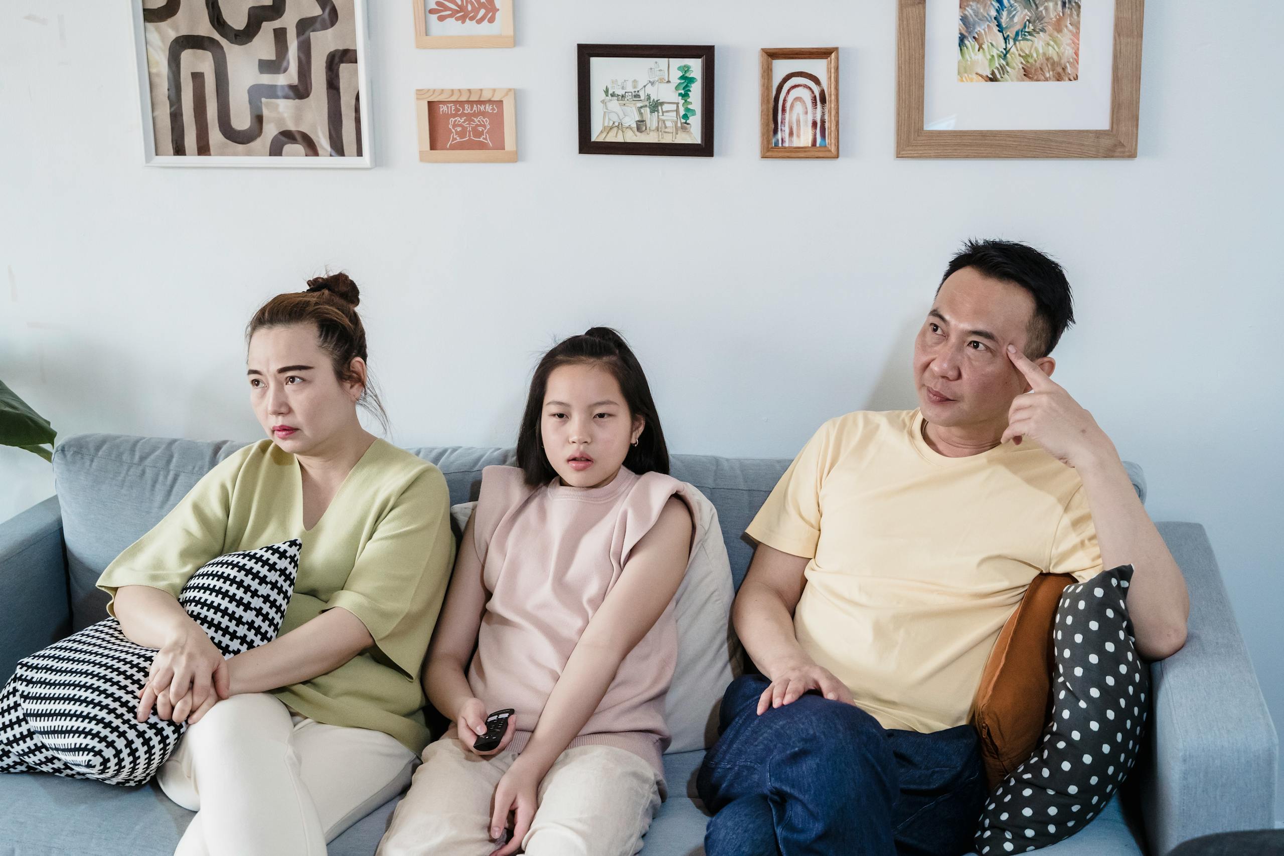 Asian family of three sitting together indoors, sharing a calm moment on the couch.