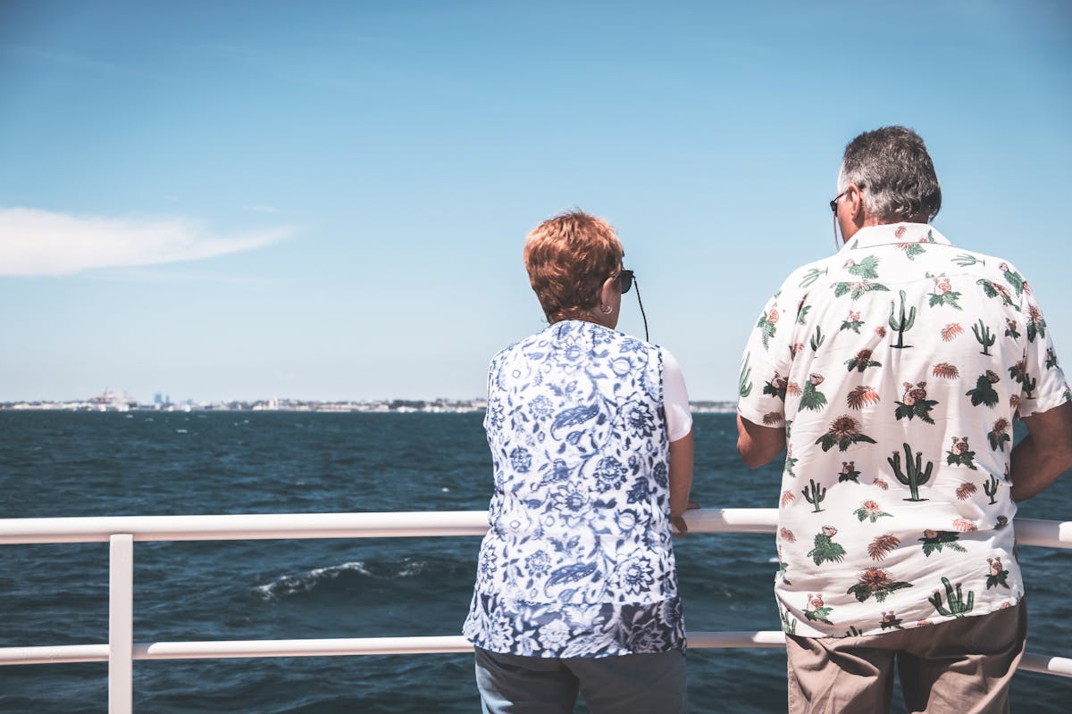 Back view of unrecognizable mature male and female travelers in casual clothes and sunglasses admiring sea during cruise on boat on sunny day