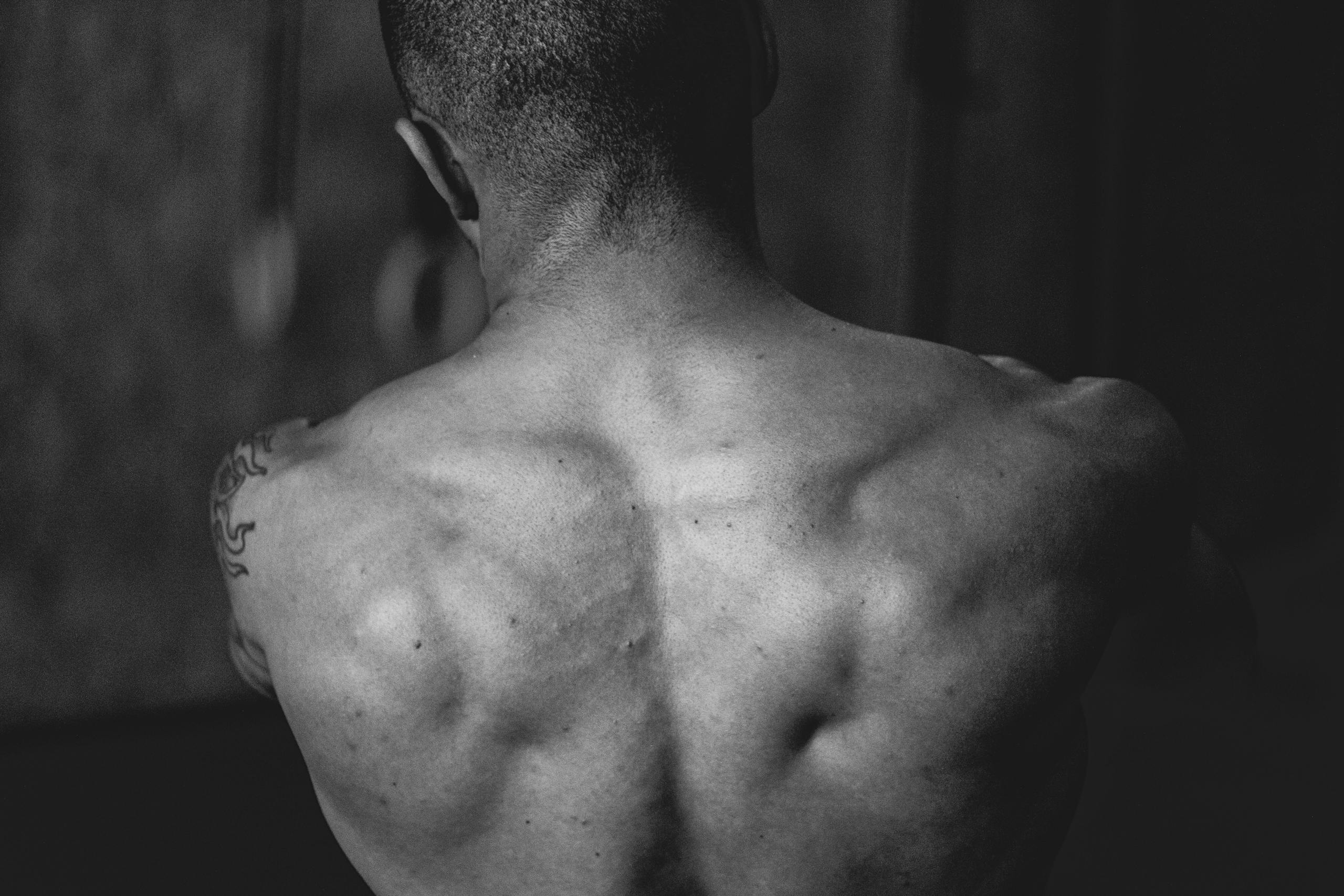 Black and white image showcasing the muscular back of a shirtless man, highlighting strength and fitness.