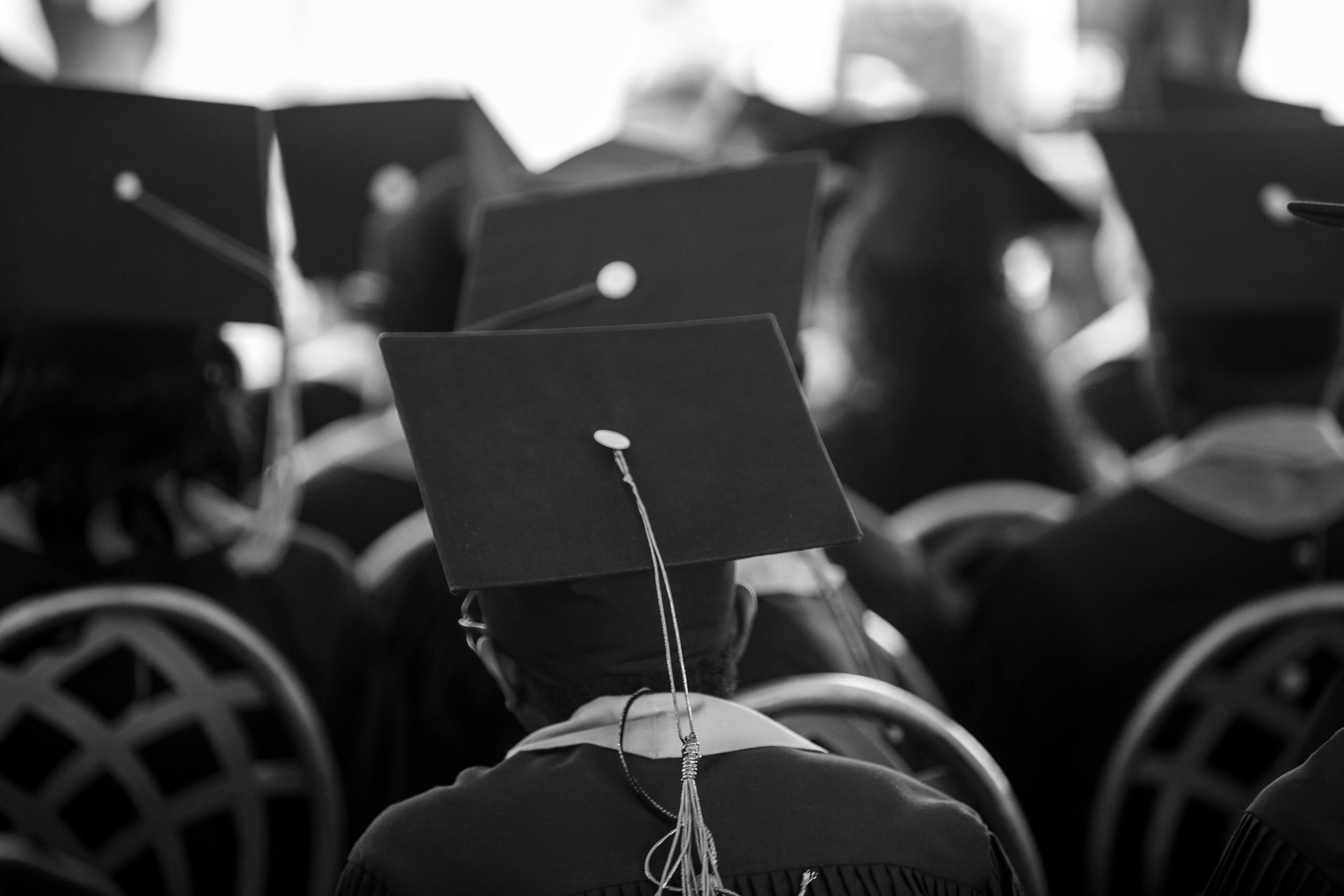 9 Brutal Ways Student Loans Are Still Controlling American Adults 2 Black and white photograph of students wearing mortarboards at a graduation ceremony.