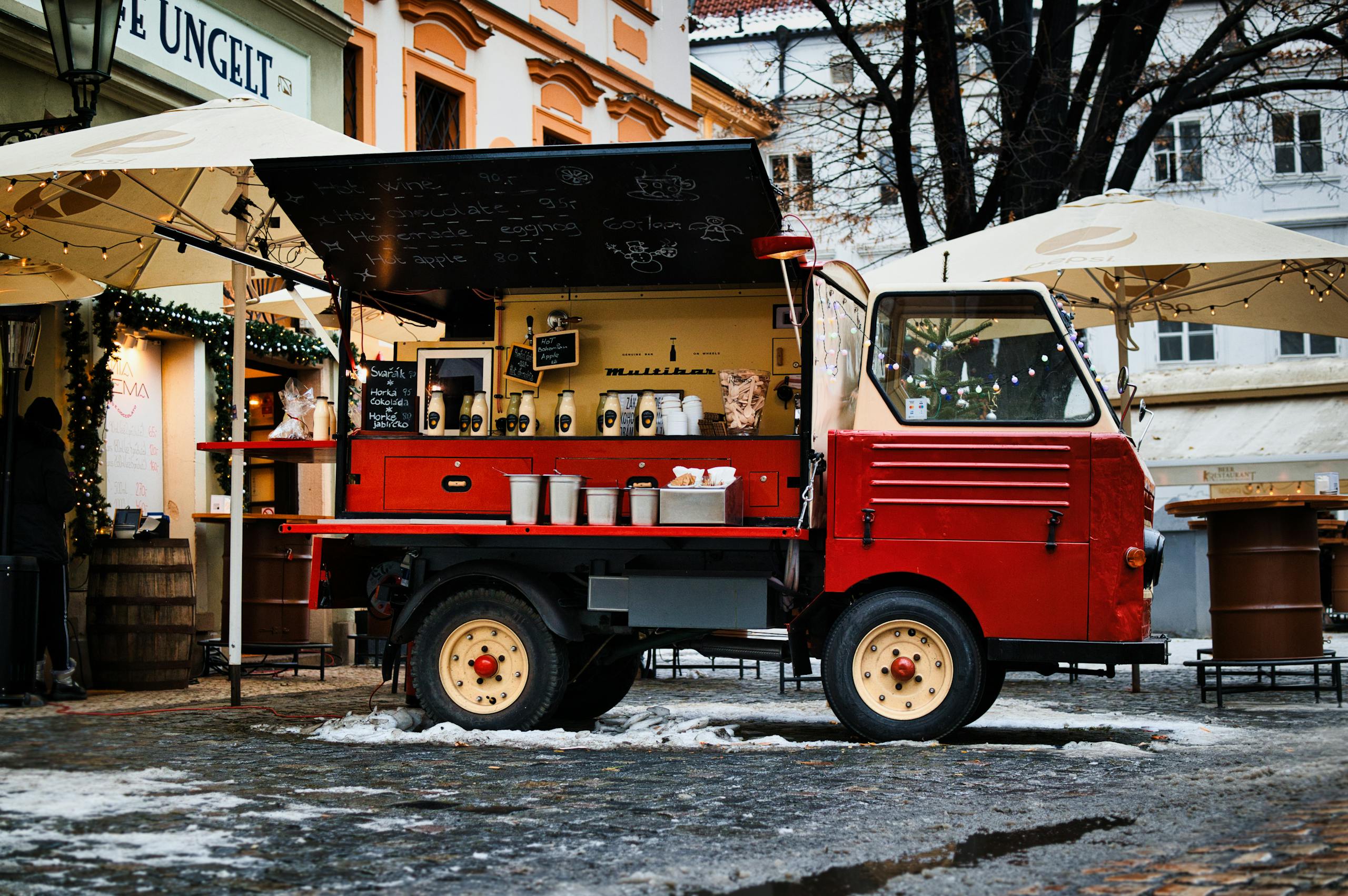 7 Places Americans Are Tired of Being Asked to Tip 3 Charming vintage red food truck serving on a snowy cobblestone street in a bustling urban winter setting.