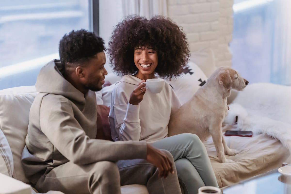 7 Signs Women Quietly Pull Back When Love Turns Into Resentment 1 Cheerful young African American couple in stylish hoodies communicating and drinking coffee while resting on comfortable couch with cute bed