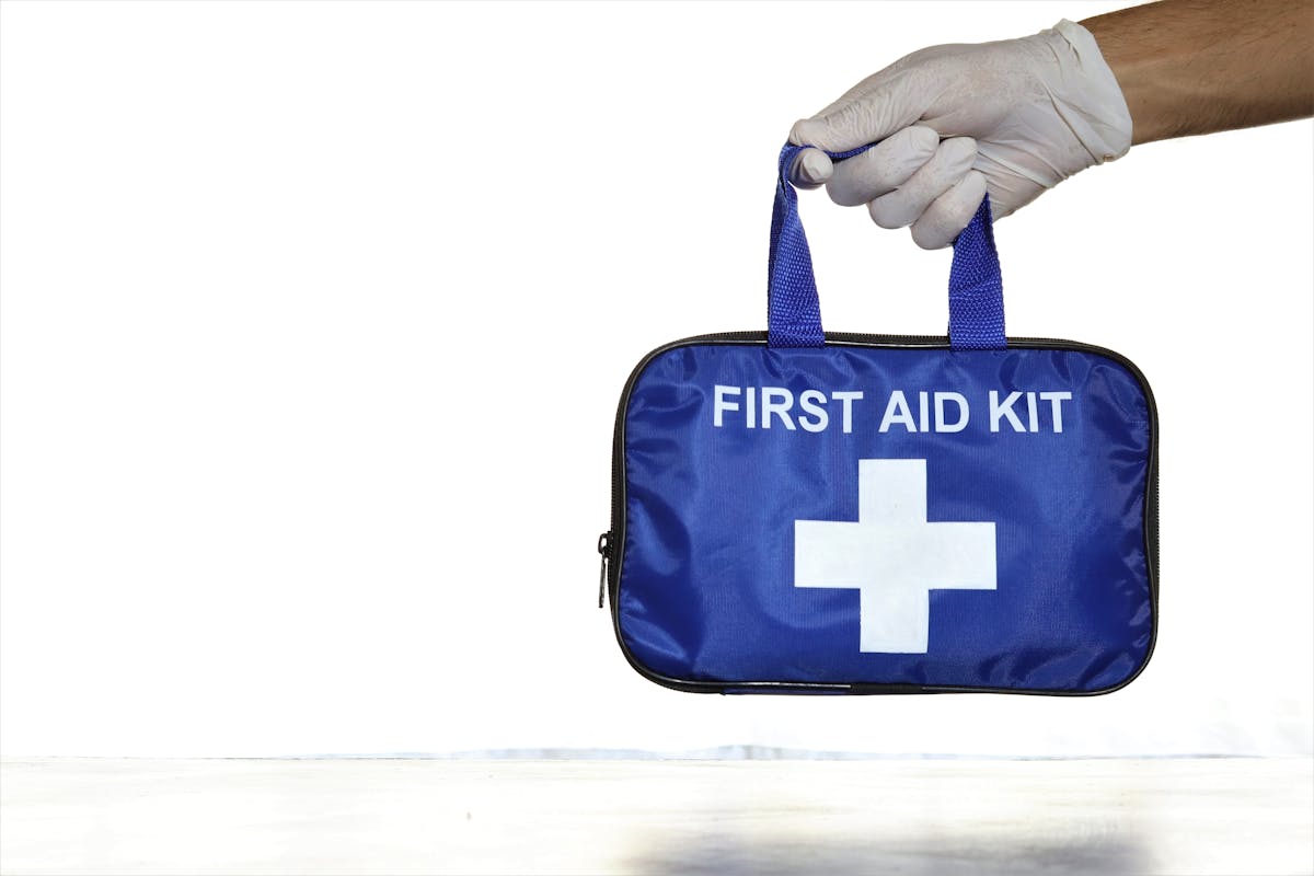 By Not Having These 12 Items ,You Are Risking Your Home’s Safety 1 Close-up of a blue first aid kit held by a hand in a latex glove against an isolated white background.