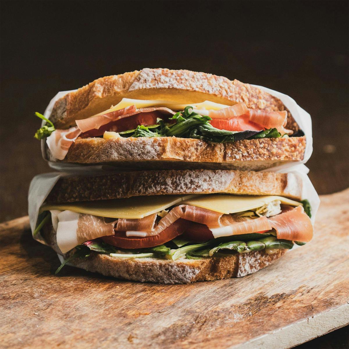 Subway Customer Demands Refund After Dispute Over Toasting Charge 1 Close-up of a gourmet sandwich with prosciutto, cheese, and greens on a wooden board.