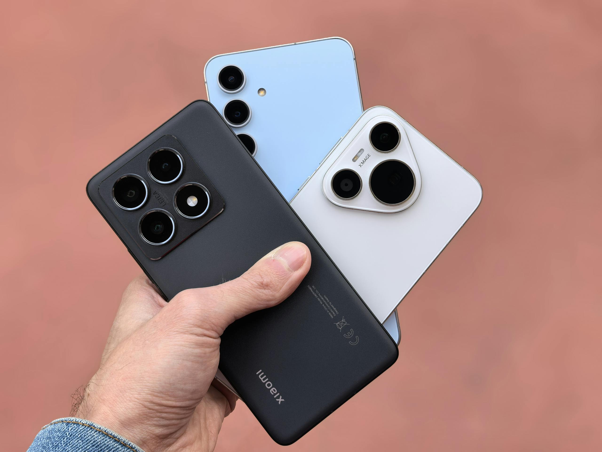 Close-up of a hand holding three modern smartphones with cameras in view, showcasing contemporary design.