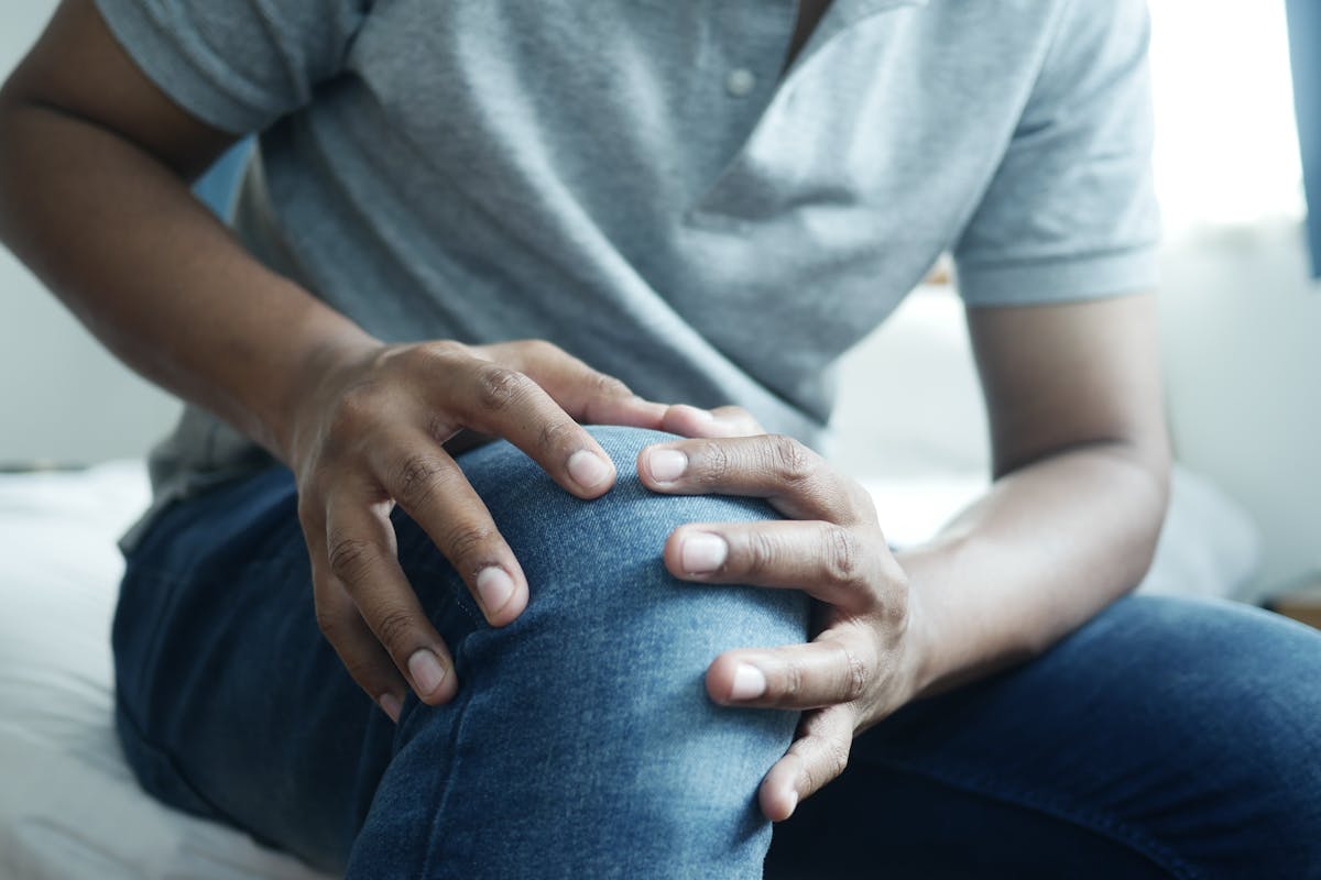 6 Symptoms You Should Never Dismiss as Normal Aging 1 Close-up of a man holding his knee, capturing a moment of discomfort in a casual indoor setting.
