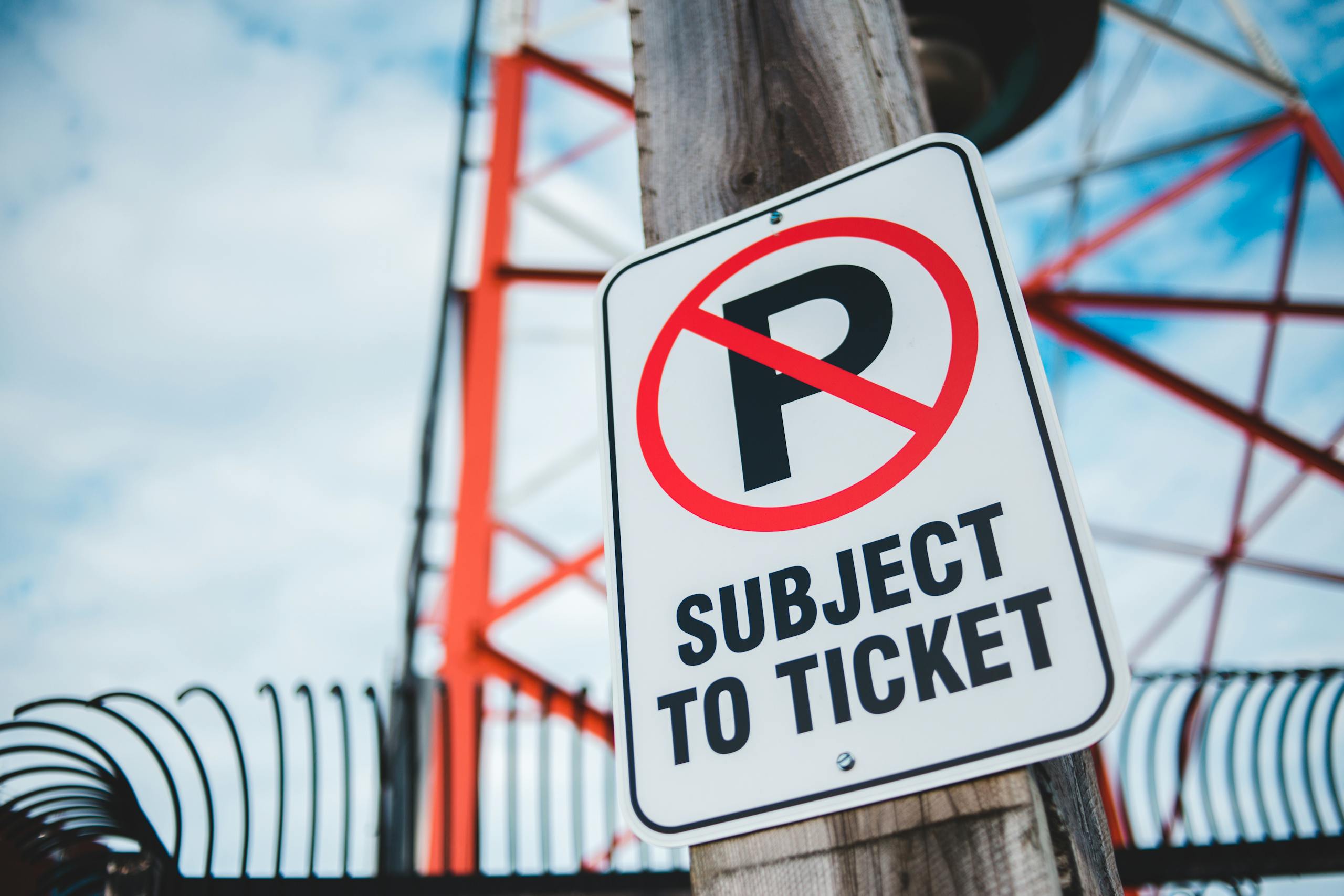 10 Junk Fees Americans Hate Paying 4 Close-up of a no parking sign with a tower in the background, emphasizing traffic restrictions and warnings.