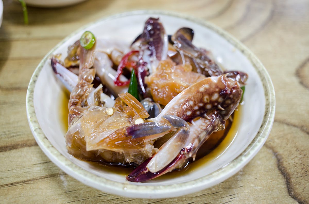 Close-up of a seafood dish with fresh crab marinated in soy sauce, sitting on a wooden table.