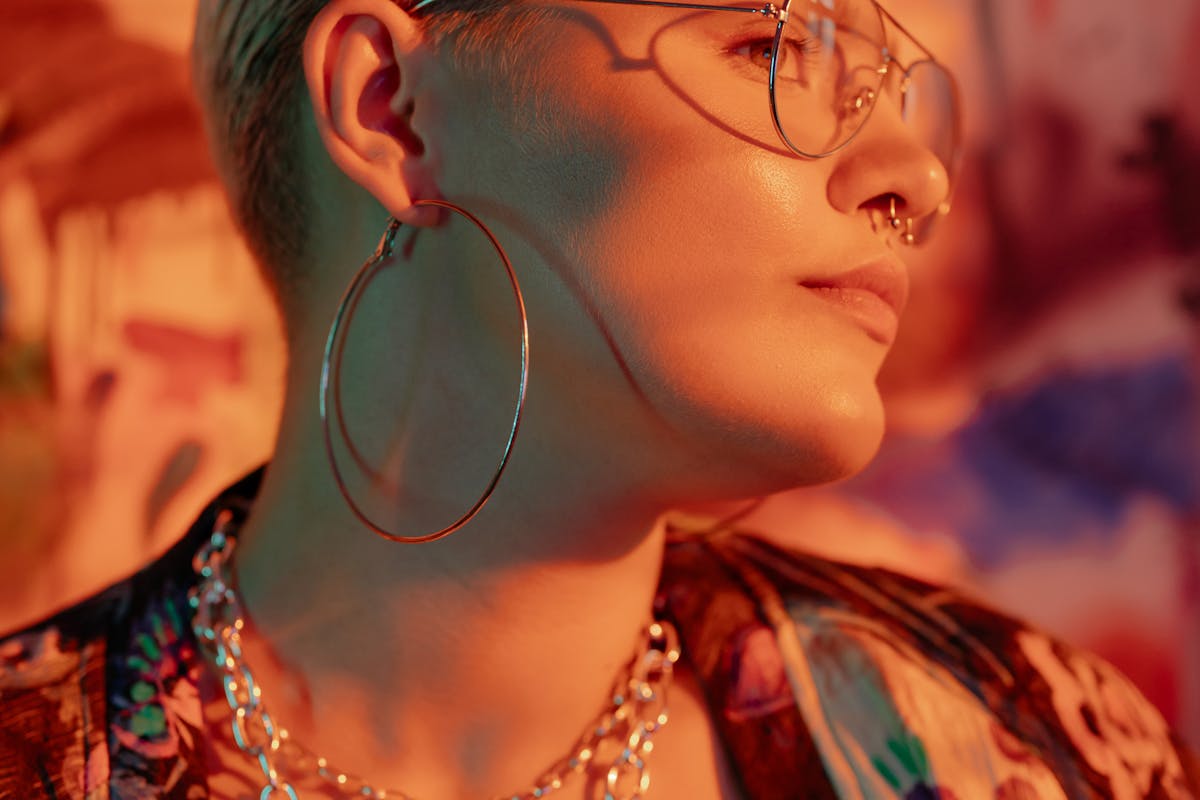 Close-up of a stylish woman wearing modern eyewear and accessories, illuminated by warm light.