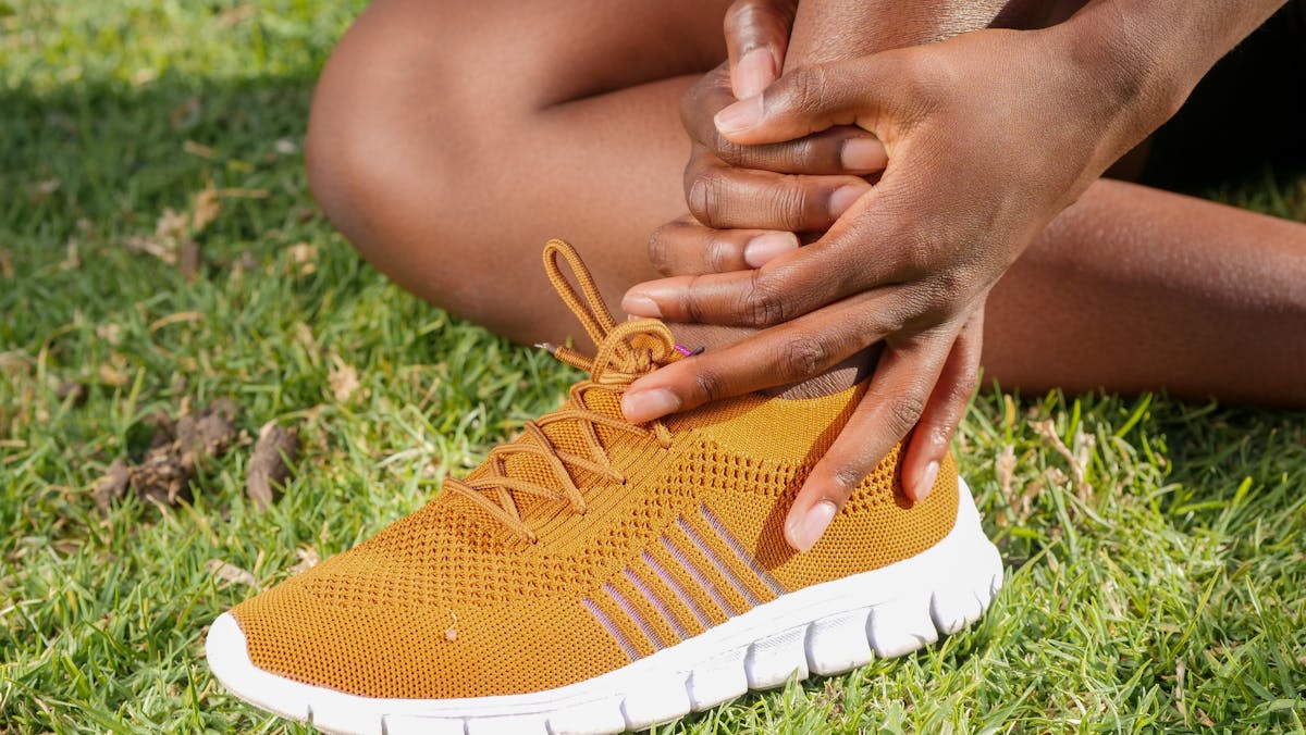 10 Sneaky Reasons You Smell Bad Without Realizing It 3 Close-up of athlete holding ankle with running shoe on grass, indicating pain or injury.