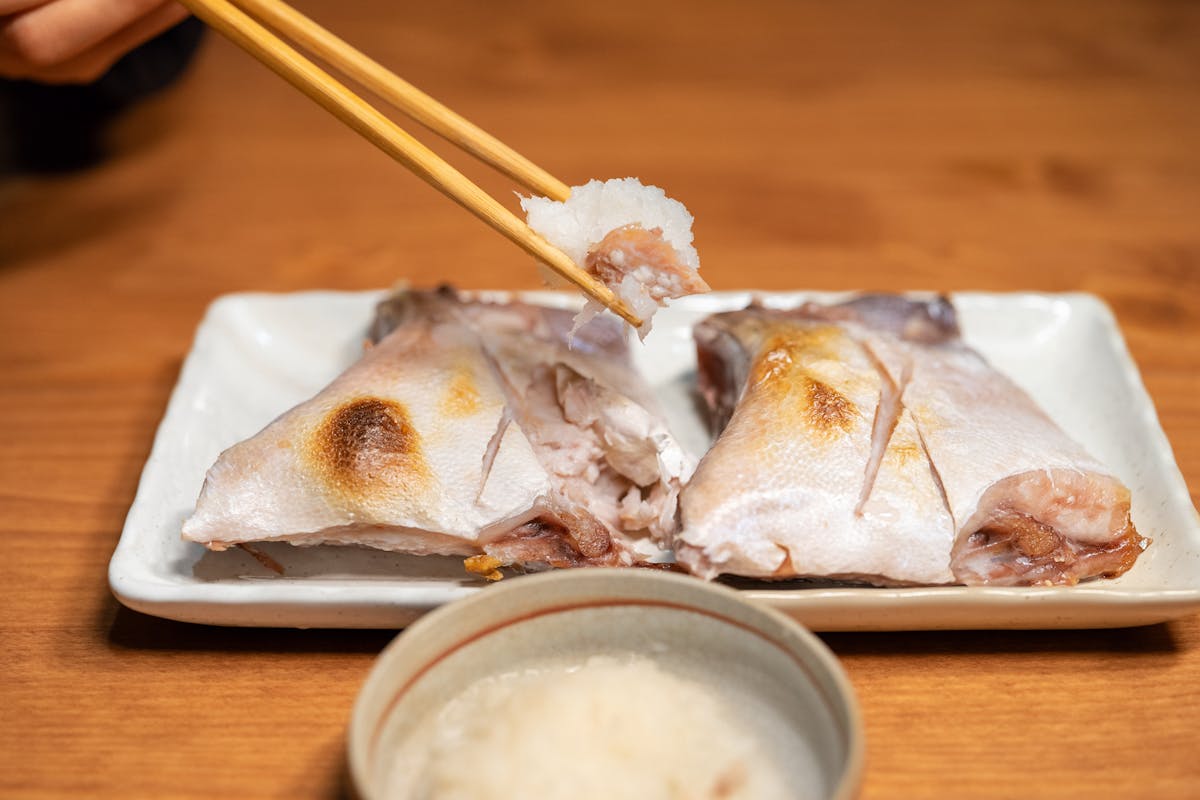 Close-up of grilled fish being served with chopsticks, highlighting traditional Asian cuisine.