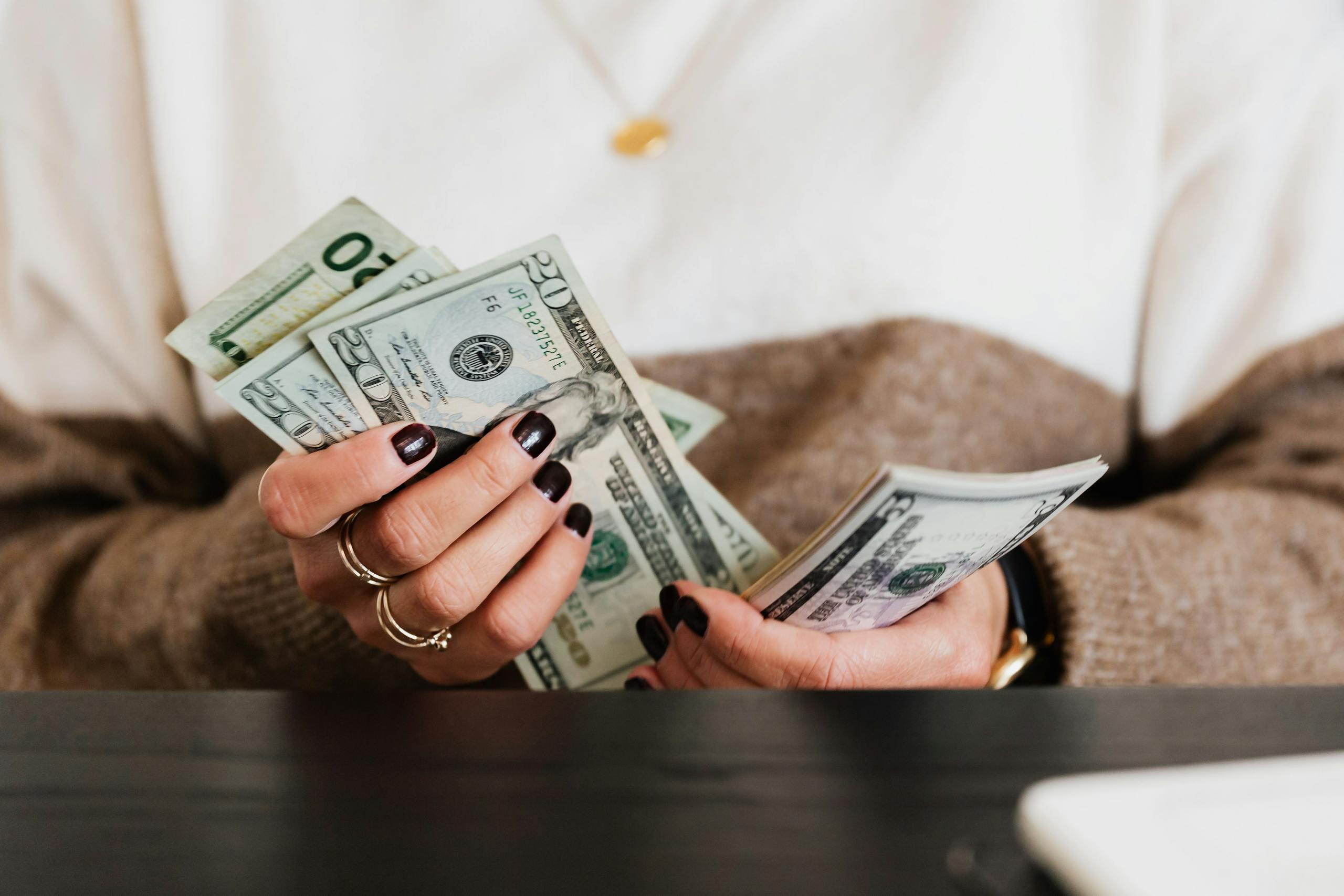 7 Types of Women Insecure Men Can’t Handle 2 Close-up of hands counting US dollar bills, depicting finance and money handling.