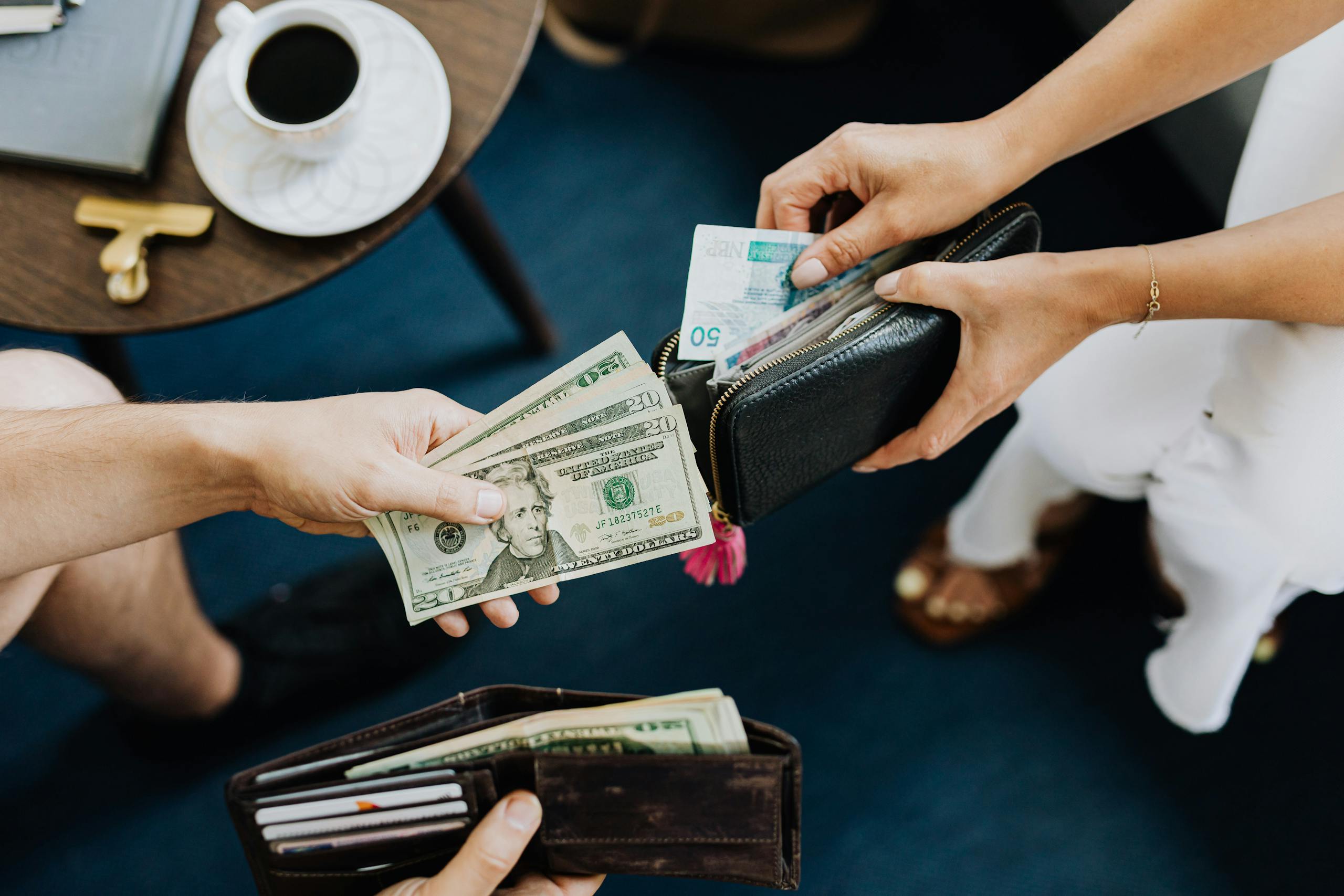 8 Brutal Dating Truths People Ignore 4 Close-up of two people exchanging US dollars and currency with wallets on a table.