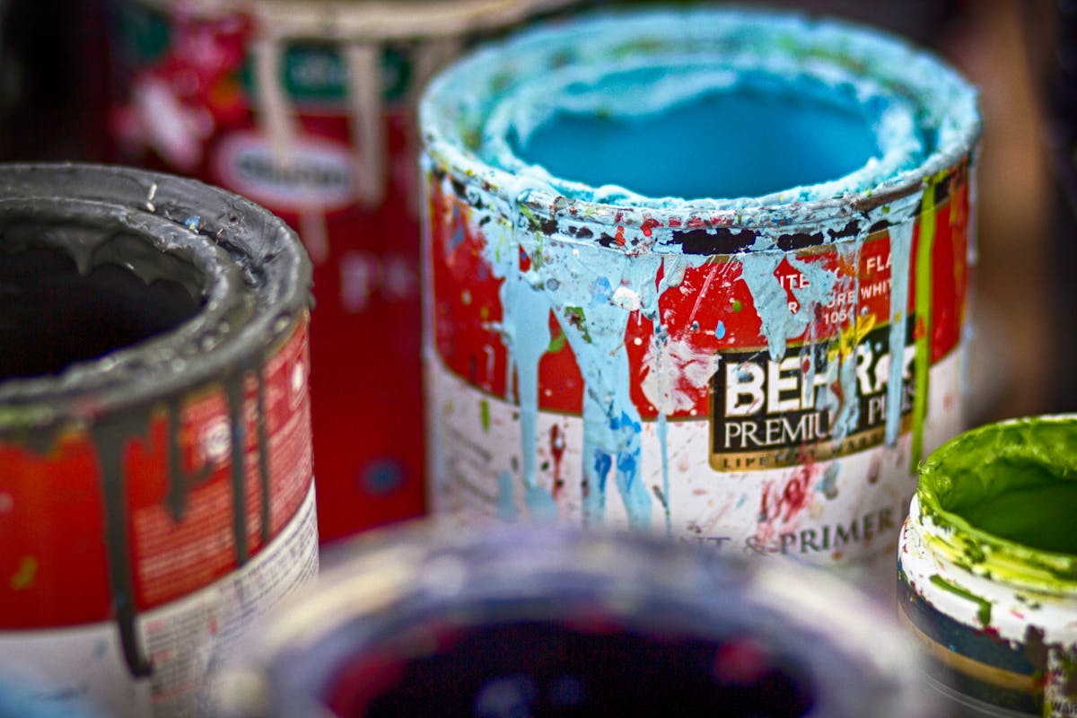Close-up of vibrant, messy open paint cans with colorful splatters on a workshop surface.