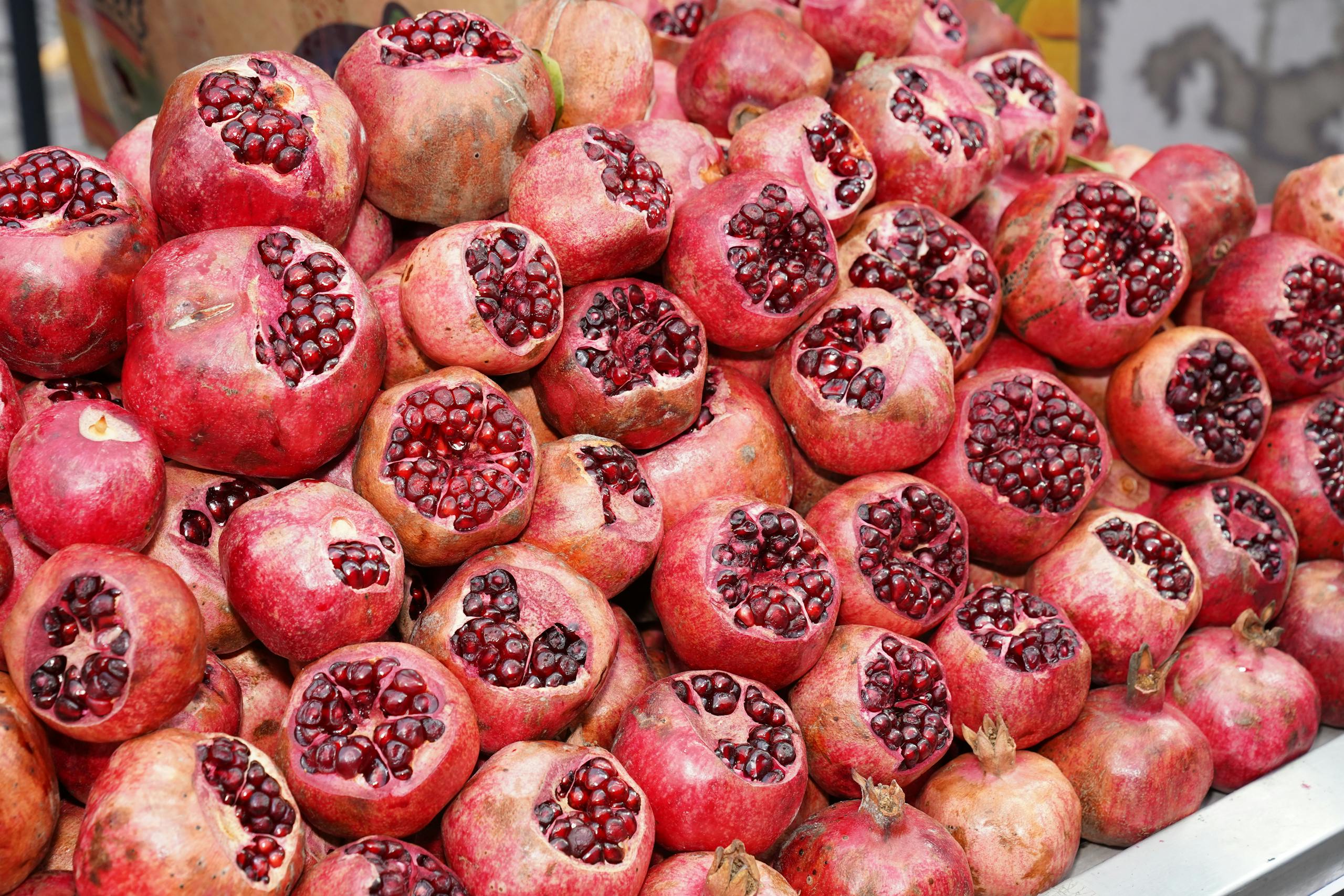 Close-up view of fresh pomegranates cut open displaying seeds at a market stall. Vibrant and juicy.