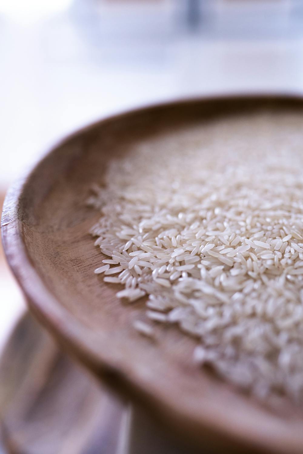 Close-up view of raw, uncooked rice grains on a rustic wooden plate. Perfect for culinary themes.