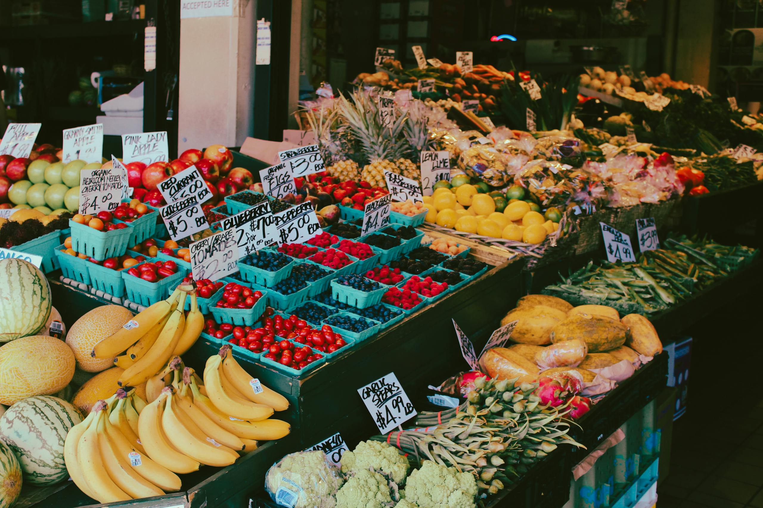 Colorful fruit and vegetable market stall displaying a variety of fresh produce with visible price tags.