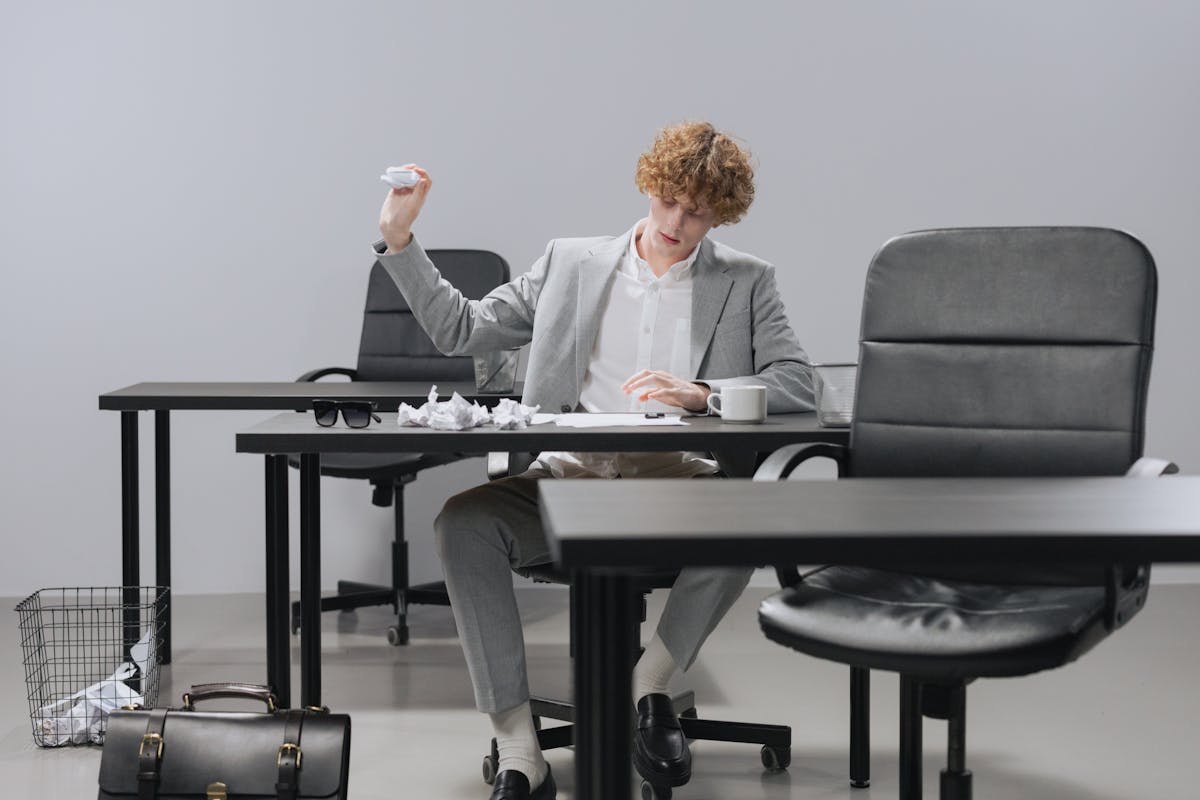 Confident young man in gray suit tossing crumpled paper in modern office setting.
