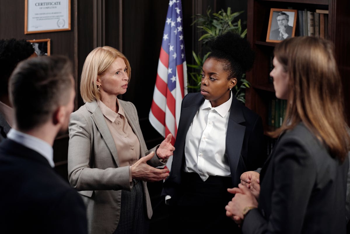 Diverse group of professionals in a discussion in a formal setting with an American flag.