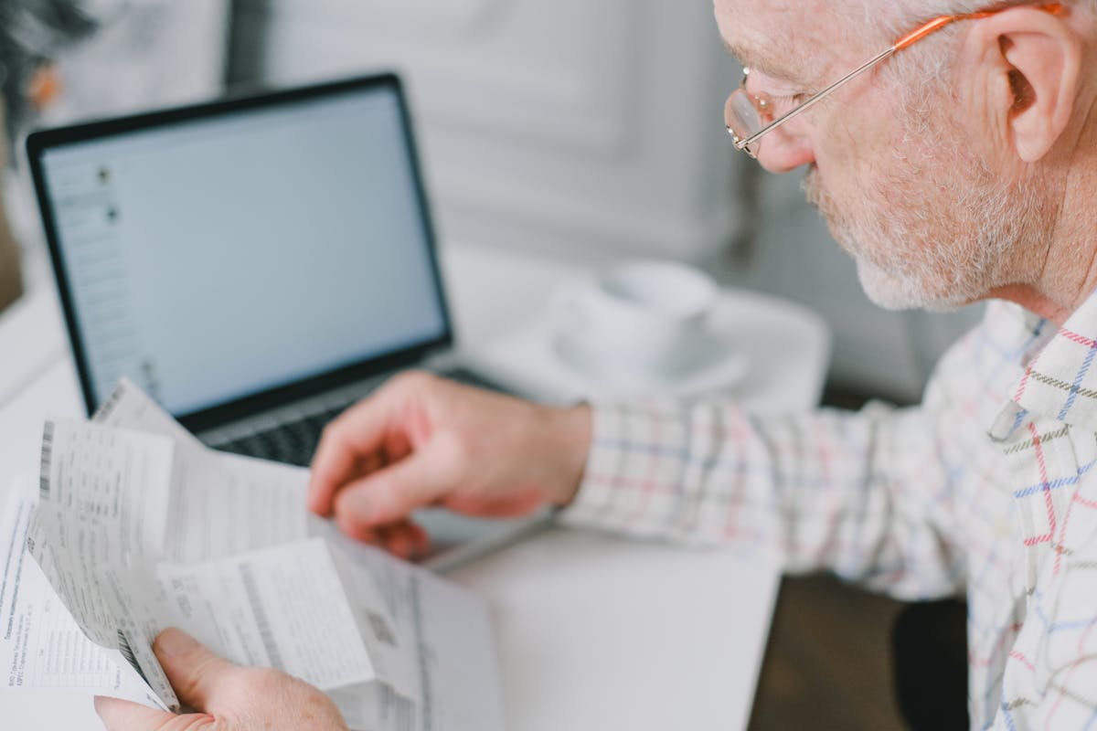9 beliefs Gen X still holds that no longer apply today 2 Elderly man wearing eyeglasses reading documents next to a laptop at home.