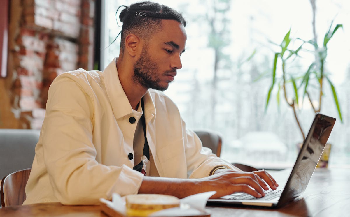 Focused young man working on a laptop in a cozy cafe setting.