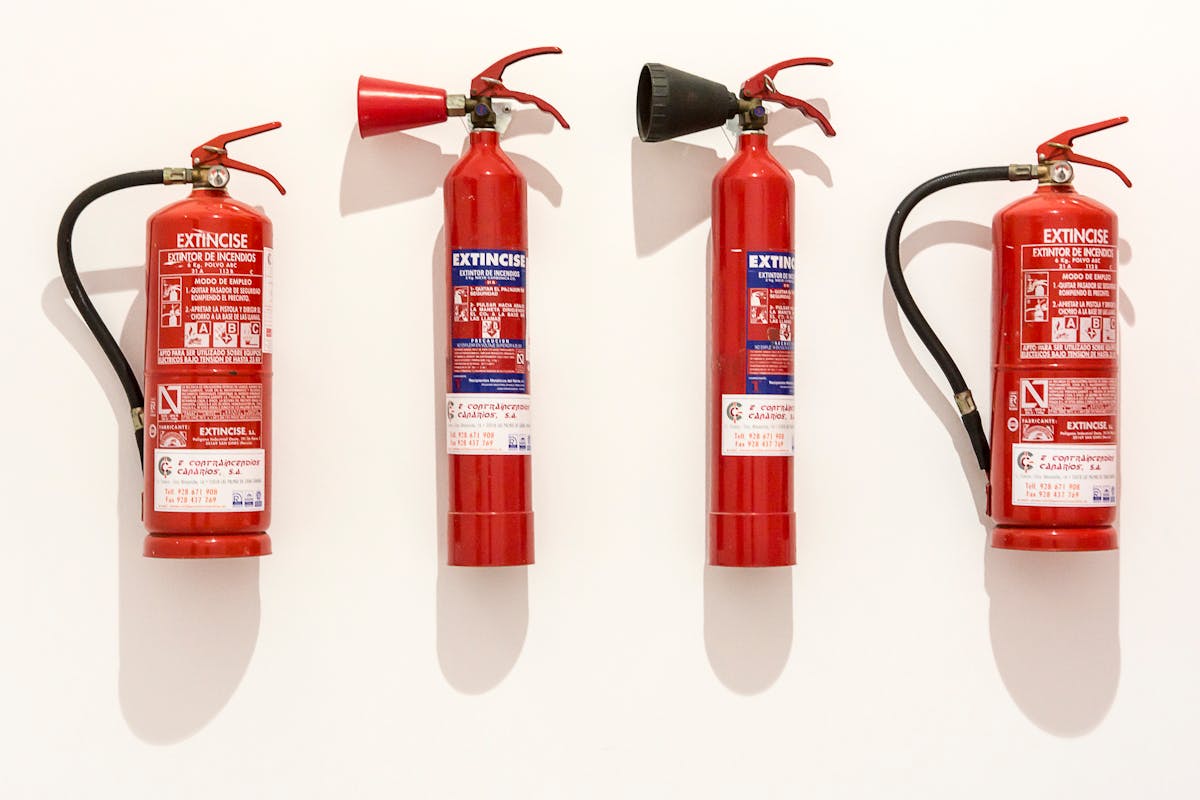 By Not Having These 12 Items ,You Are Risking Your Home’s Safety 3 Four red fire extinguishers hanging on a clean white wall in an orderly fashion.